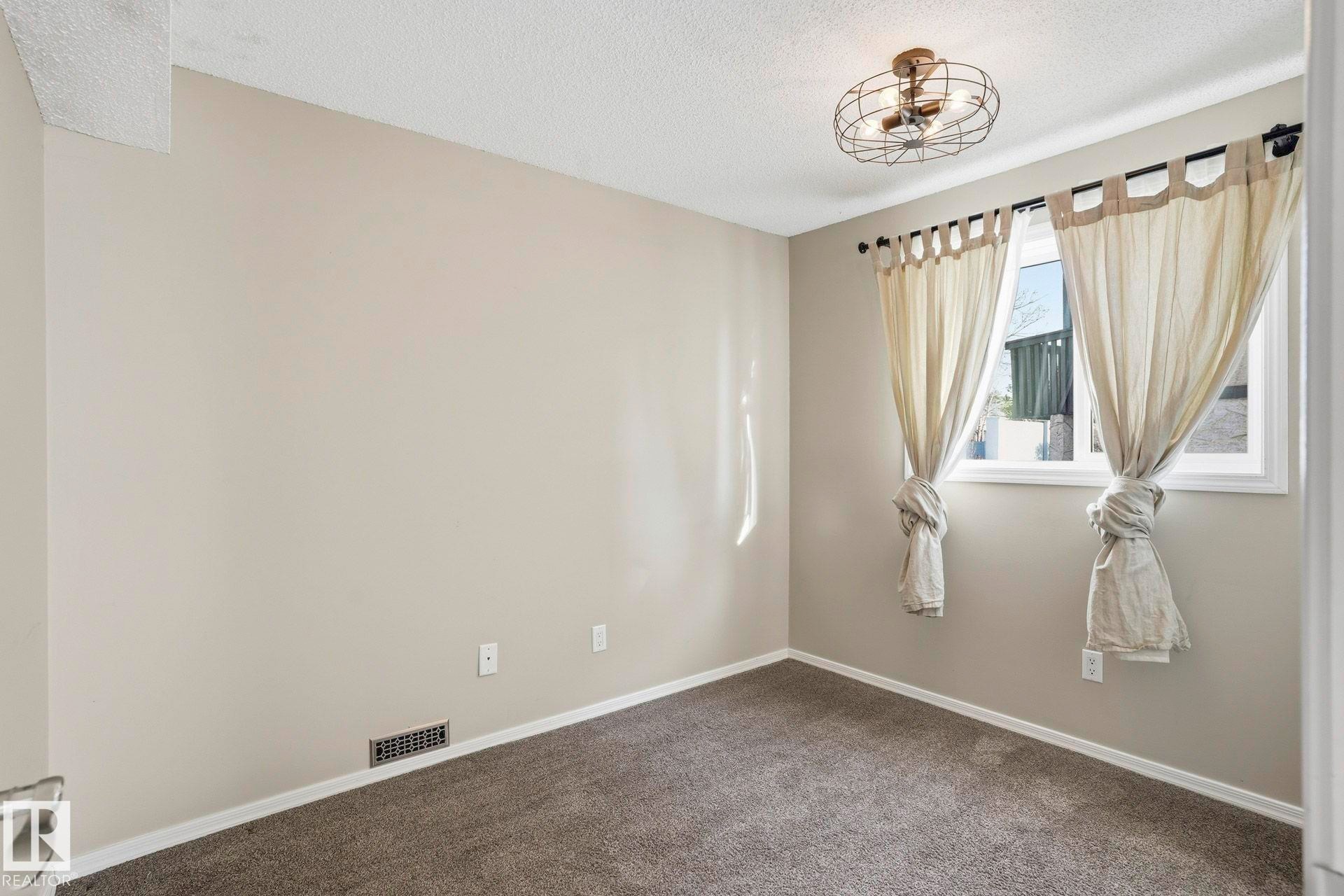Empty room with a textured ceiling and dark carpet - Edmonton, AB - Indoor Photo Showing Other Room