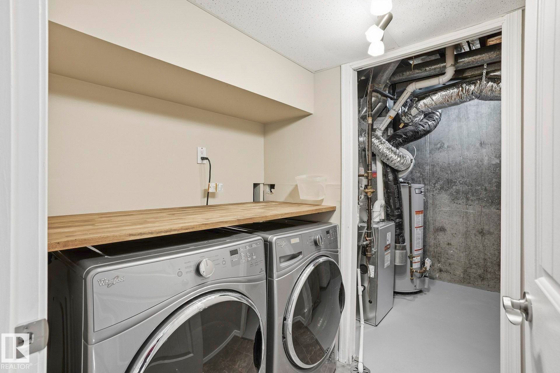 Laundry area with concrete floors, separate washer and dryer, water heater, and a heating unit - Edmonton, AB - Indoor Photo Showing Laundry Room