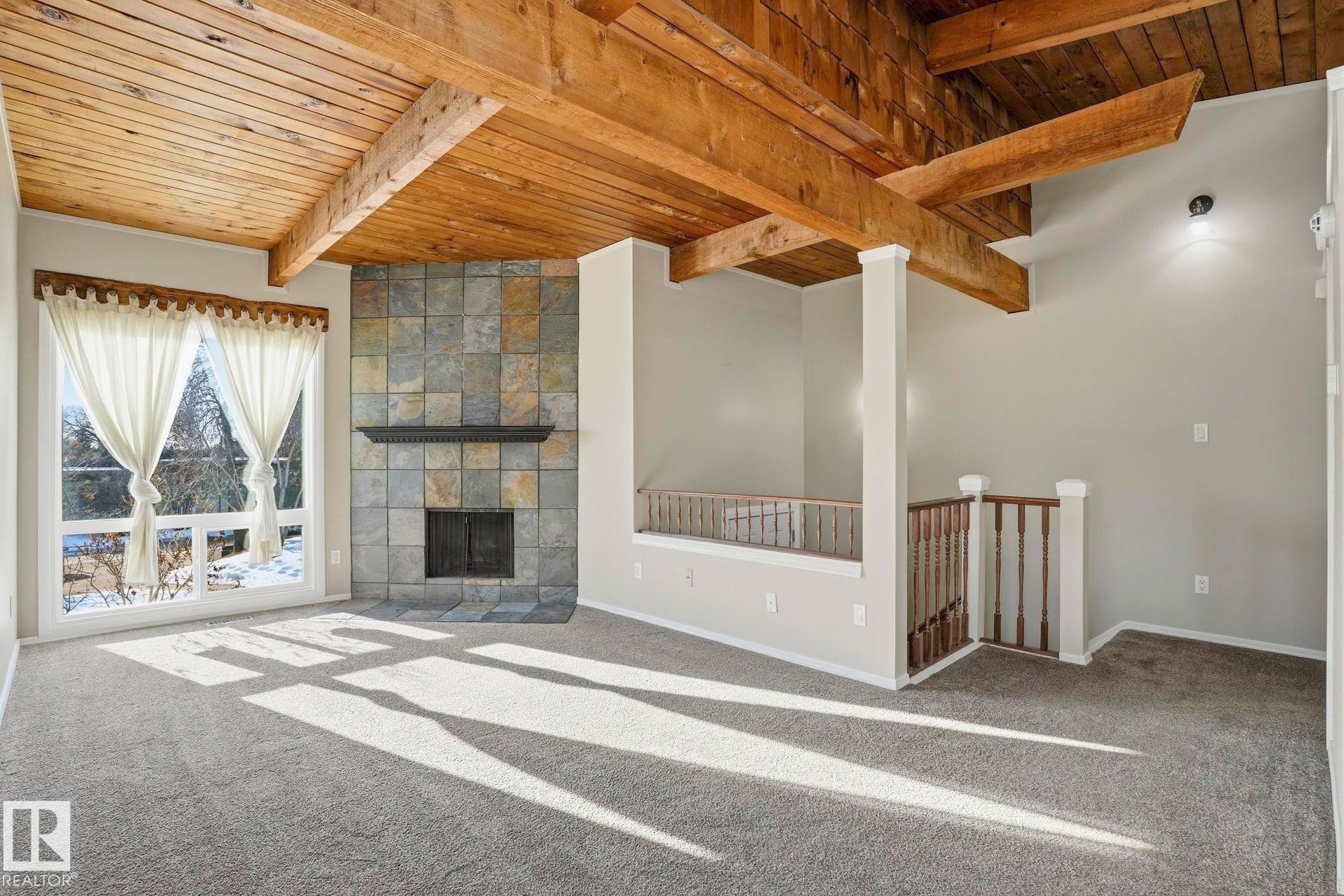 Unfurnished living room featuring a fireplace, carpet flooring, and a wood ceiling with exposed beams - Edmonton, AB - Indoor With Fireplace