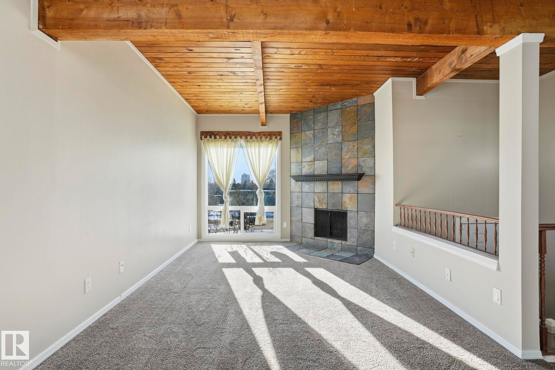 Unfurnished living room with a fireplace, a wooden ceiling with exposed beams, and carpet - Edmonton, AB - Indoor Photo Showing Other Room With Fireplace