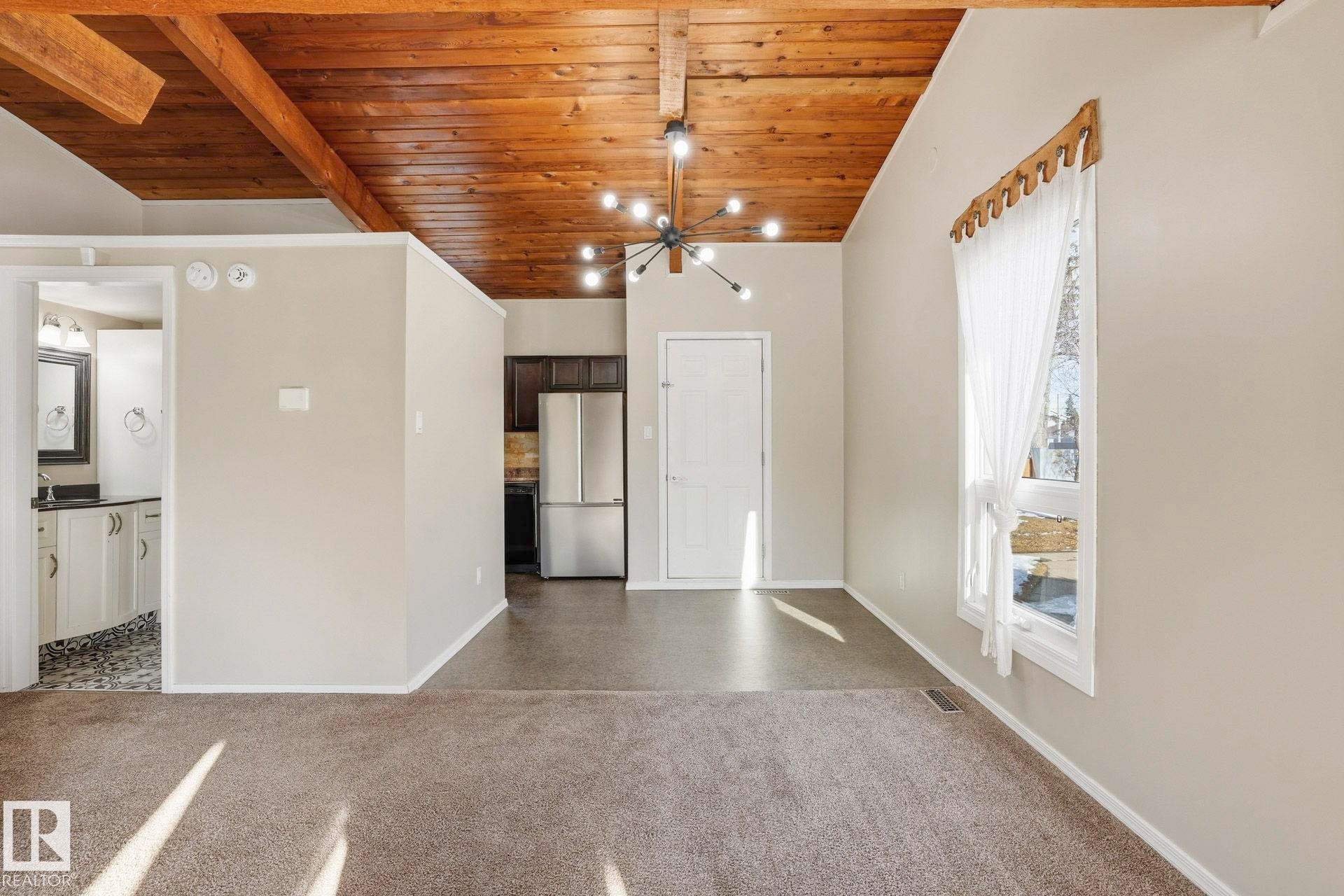 Unfurnished dining area with a wood ceiling with exposed beams, dark colored carpet, and suspended lighting - Edmonton, AB - Indoor Photo Showing Other Room