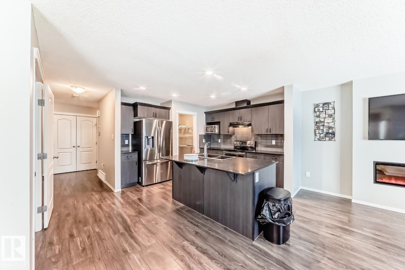 Kitchen with stainless steel appliances, dark wood finish cabinets, an island with sink, a breakfast bar area, and light wood finished floors - 2823 Duke Crescent, Edmonton, AB - Indoor Photo Showing Kitchen