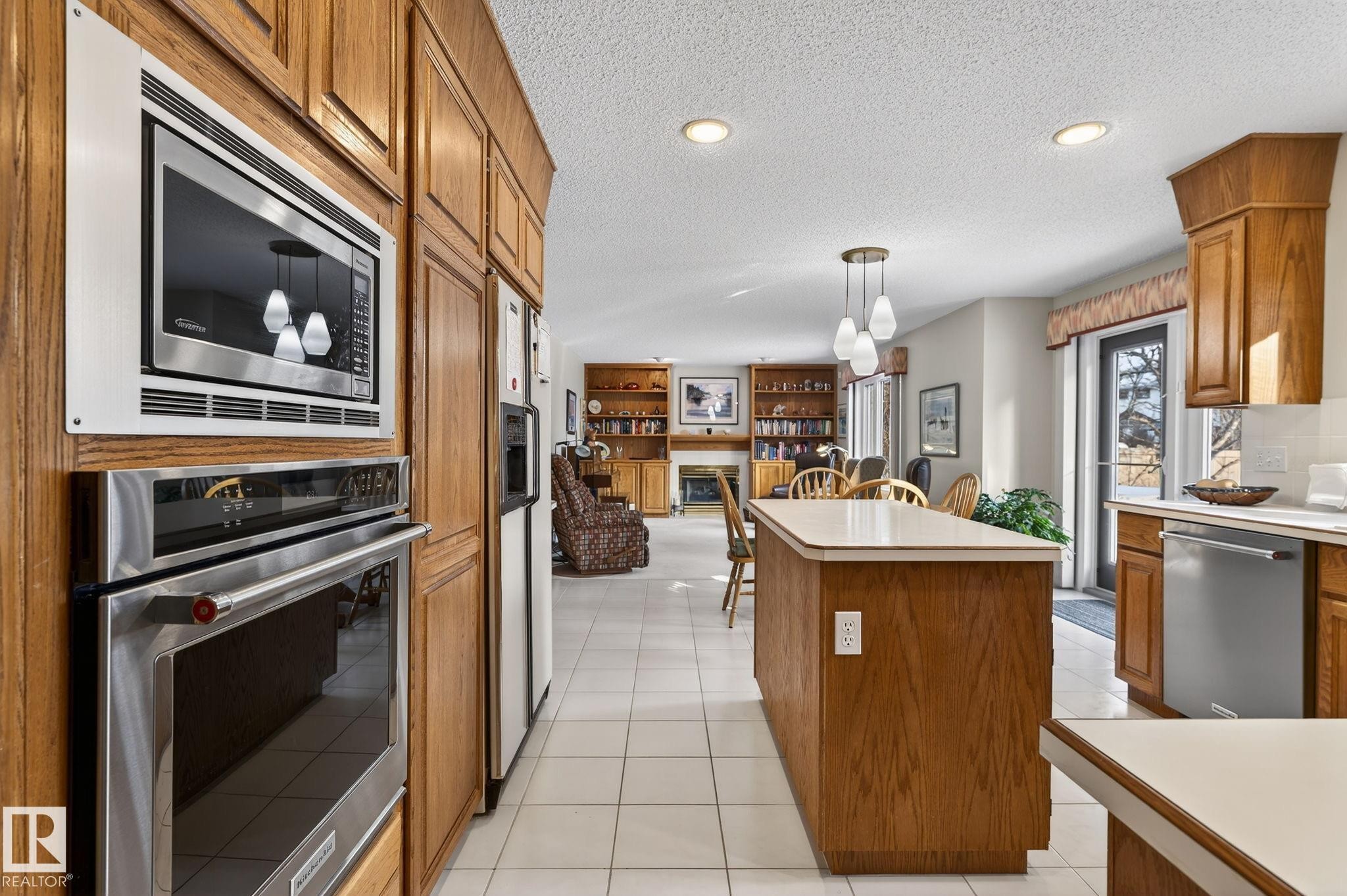 Kitchen with wood finish cabinets, hanging light fixtures, stainless steel appliances, light countertops, and light tile patterned floors - 313 Hedley Way, Edmonton, AB - Indoor Photo Showing Kitchen