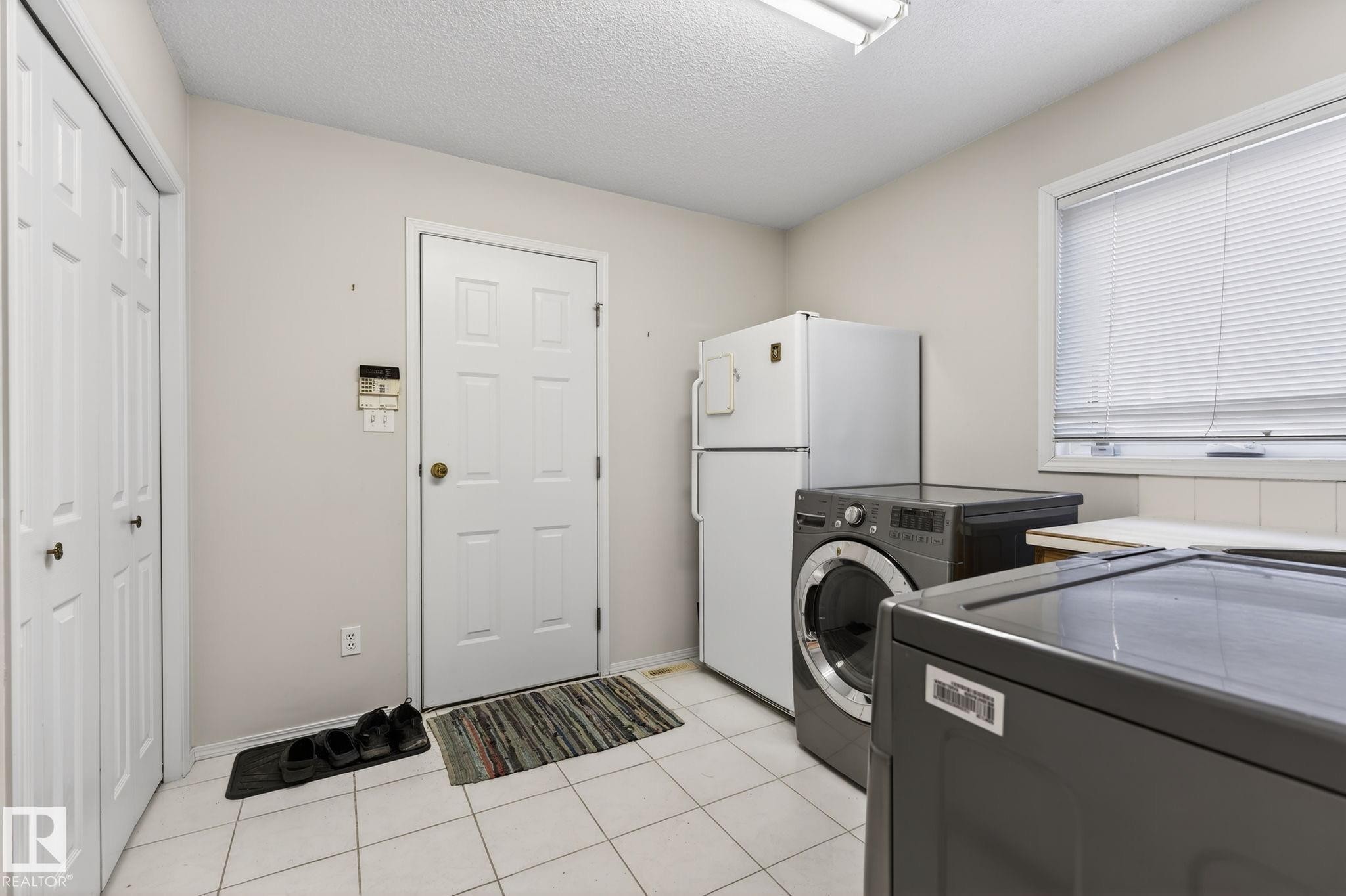 Laundry room with a textured ceiling, light tile patterned floors, and washing machine and clothes dryer - 313 Hedley Way, Edmonton, AB - Indoor Photo Showing Laundry Room
