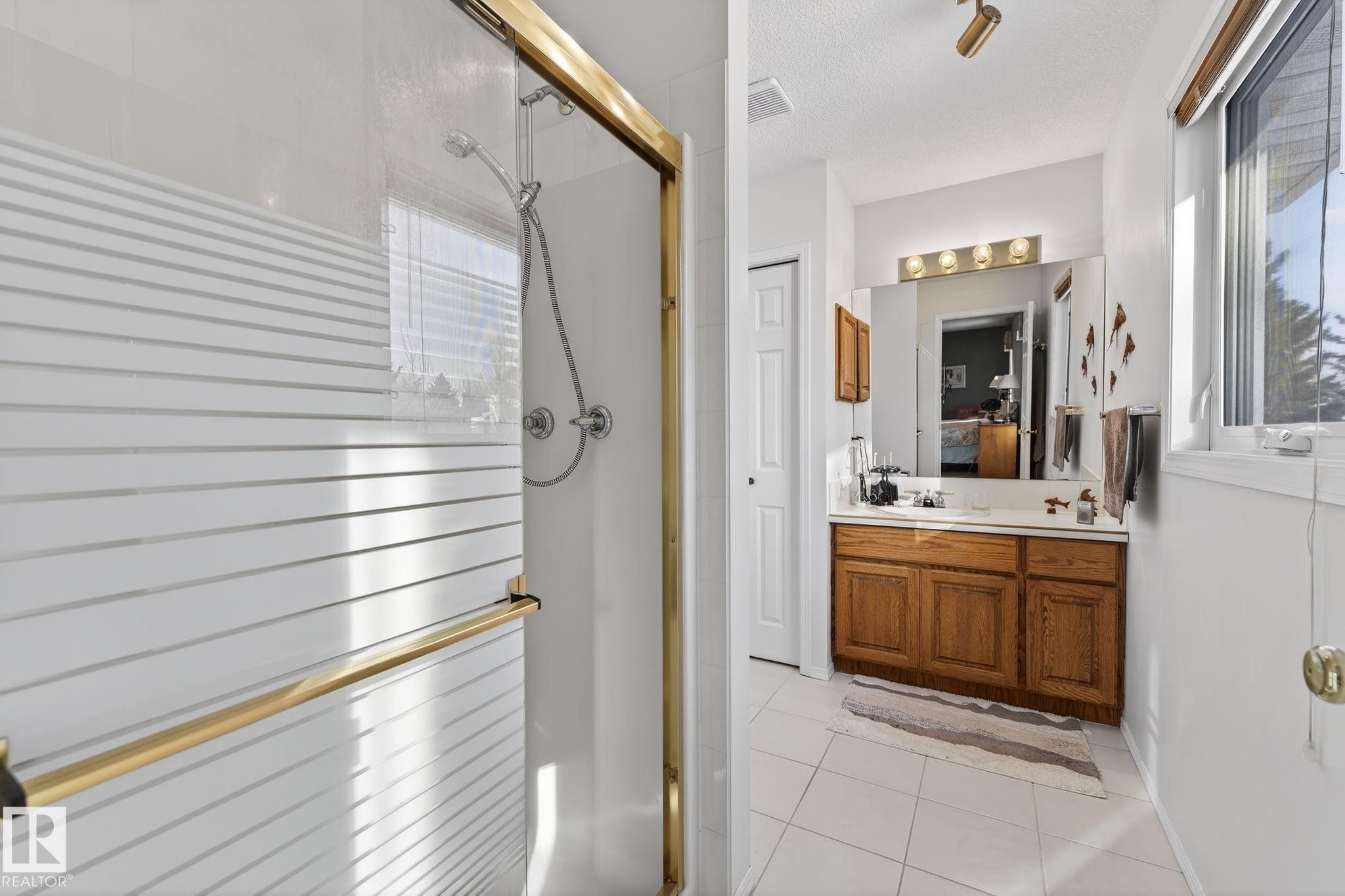 Ensuite bathroom featuring a shower stall, vanity, light tile patterned floors, and a textured ceiling - 313 Hedley Way, Edmonton, AB - Indoor Photo Showing Bathroom