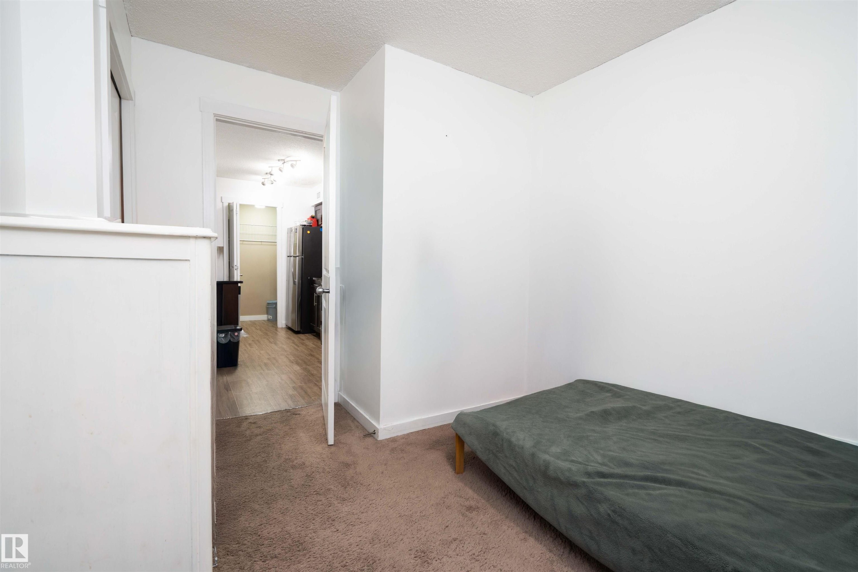 Carpeted bedroom with a textured ceiling and freestanding refrigerator - 415 111 Watt Common, Edmonton, AB - Indoor