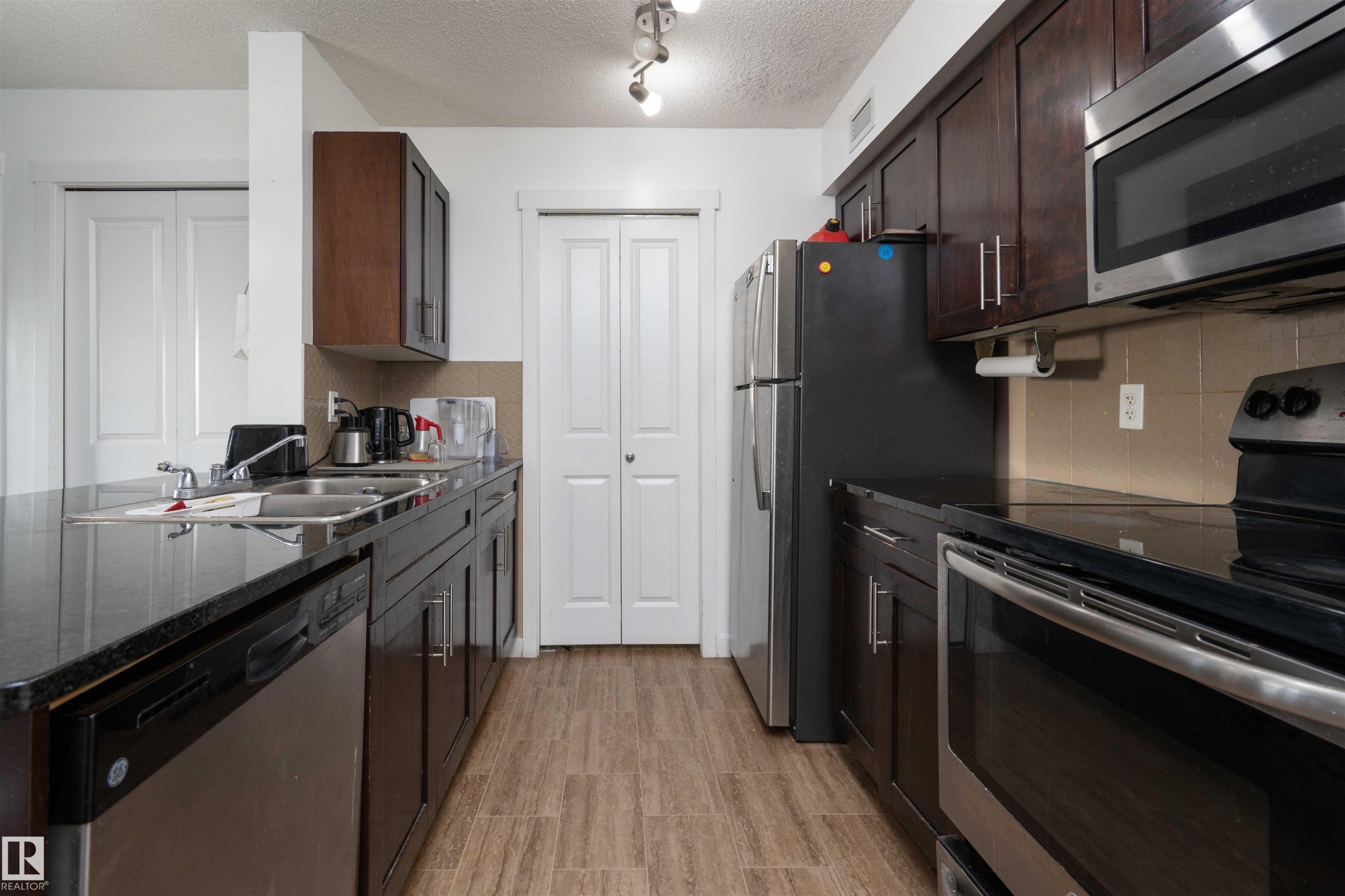 Kitchen with stainless steel appliances, a textured ceiling, dark wood finish cabinets, a peninsula, and light wood-style flooring - 415 111 Watt Common, Edmonton, AB - Indoor Photo Showing Kitchen