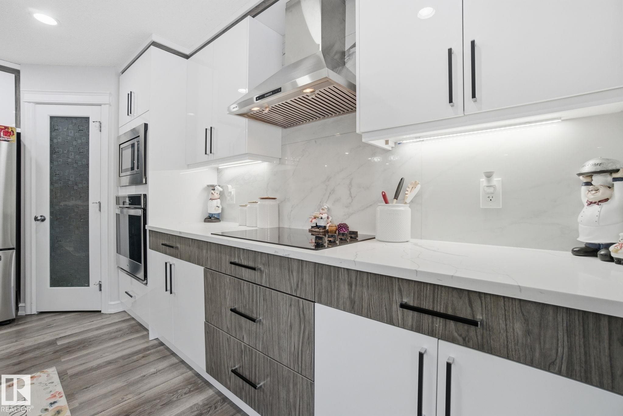 Kitchen featuring exhaust hood, white cabinetry, modern cabinets, decorative backsplash, and appliances with stainless steel finishes - 1532 37C Avenue, Edmonton, AB - Indoor Photo Showing Kitchen With Upgraded Kitchen