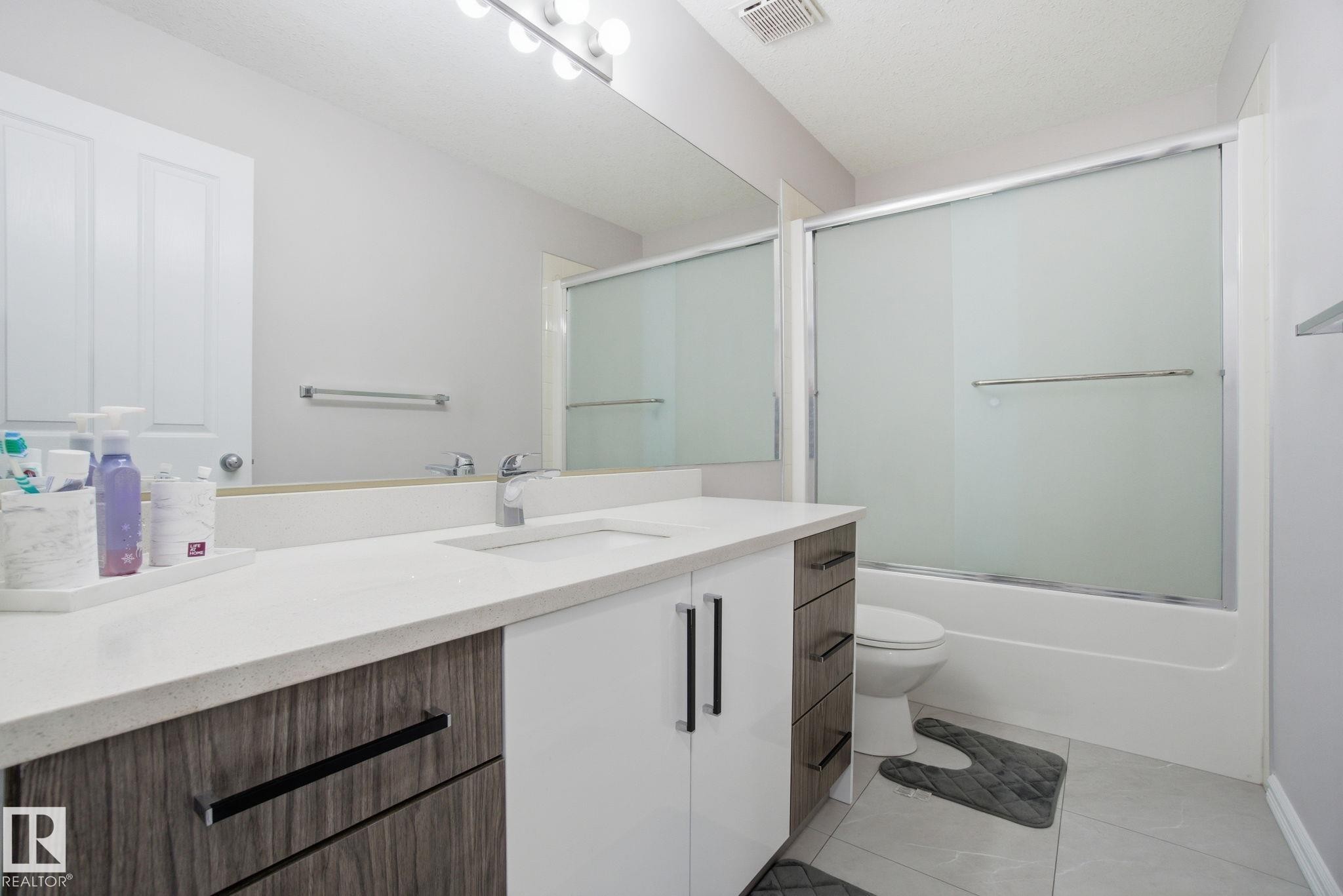 Bathroom featuring shower / bath combination with glass door, vanity, and light tile patterned floors - 1532 37C Avenue, Edmonton, AB - Indoor Photo Showing Bathroom