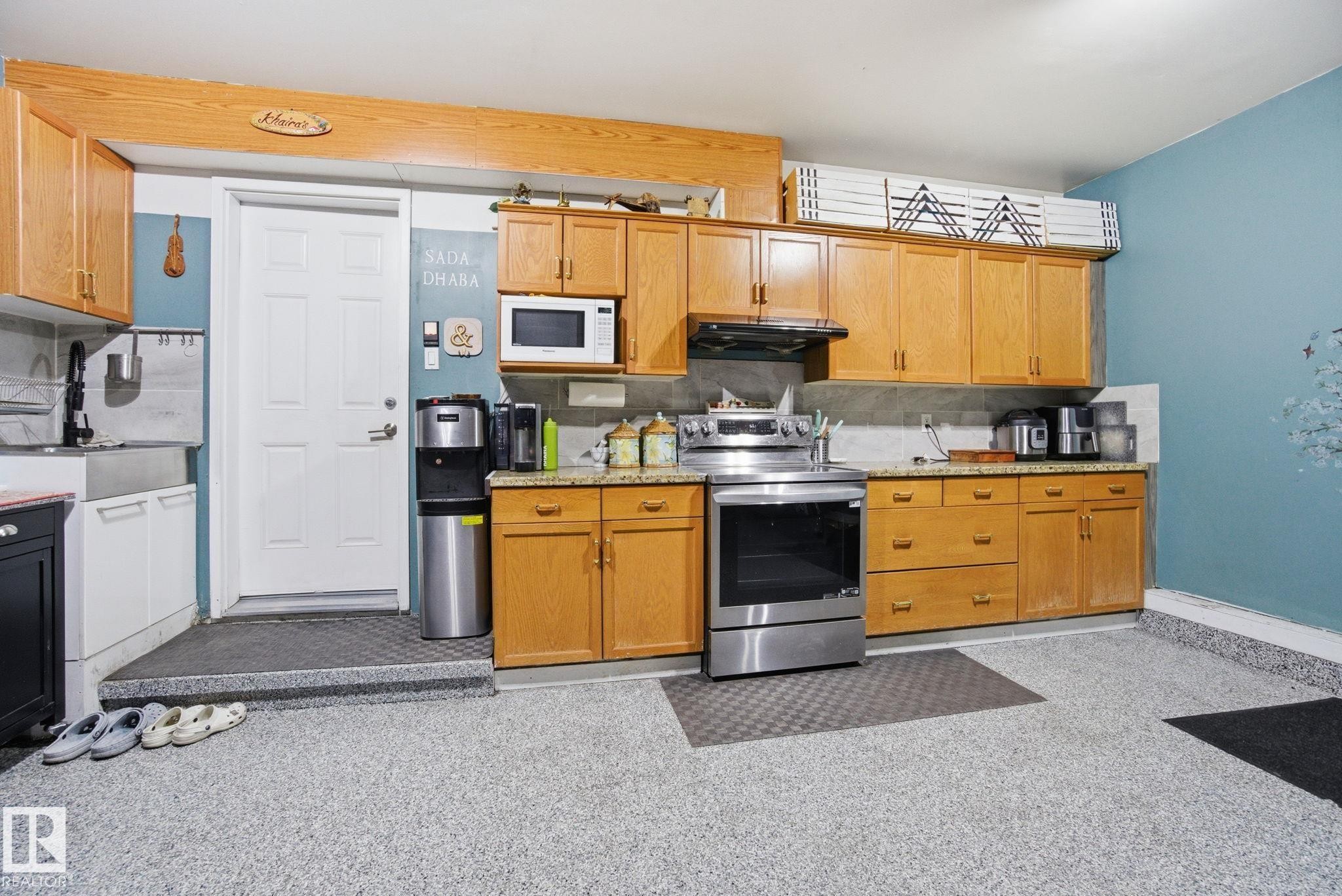 Kitchen with electric range, white microwave, tasteful backsplash, under cabinet range hood, and brown cabinets - 1532 37C Avenue, Edmonton, AB - Indoor Photo Showing Kitchen