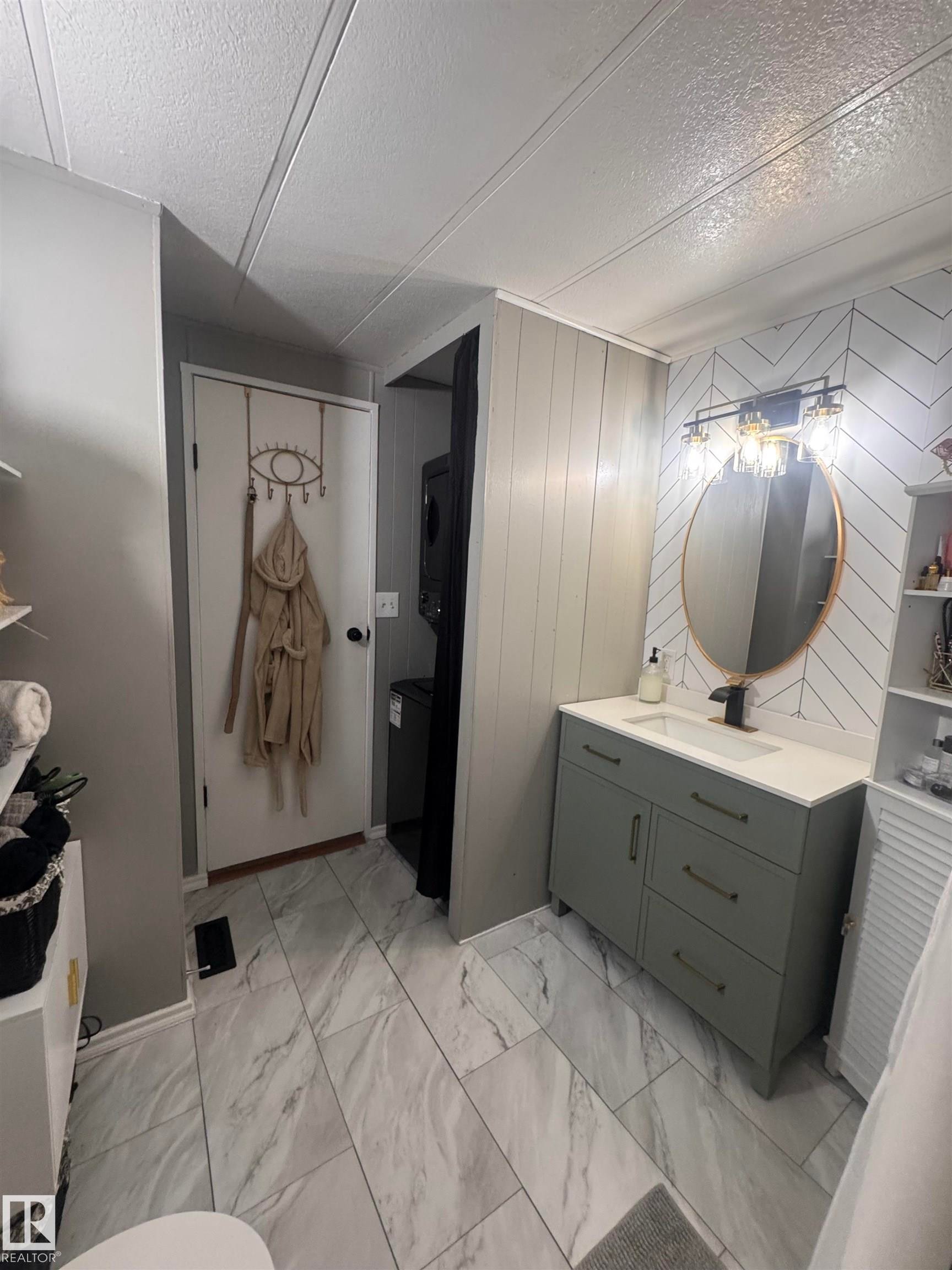 Bathroom with vanity, light marble finish flooring, wooden walls, a textured ceiling, and stacked washer and clothes dryer - #44 9501 104 Ave, Westlock, AB - Indoor Photo Showing Bathroom