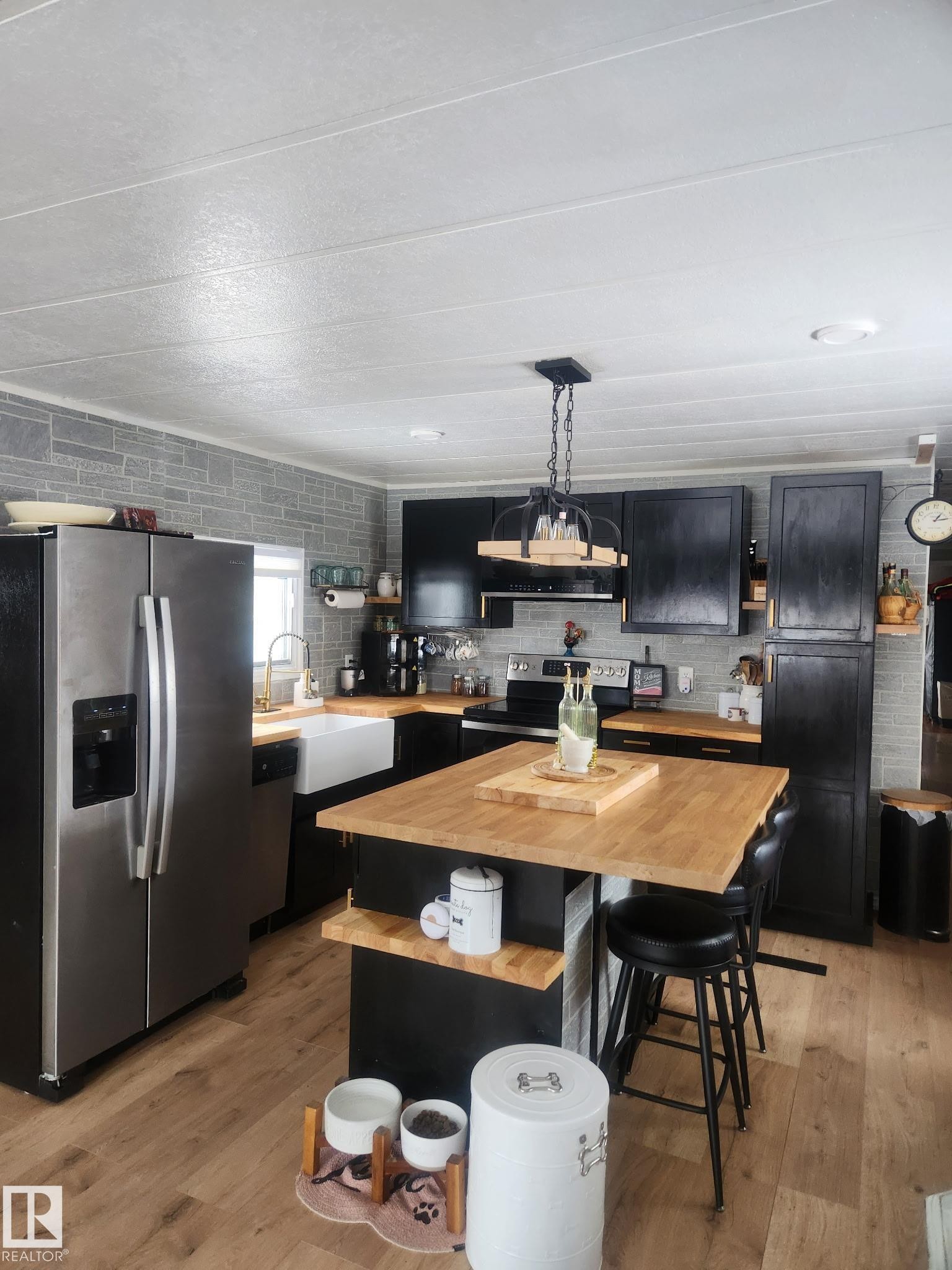 Kitchen with dark cabinetry, stainless steel appliances, a center island, decorative light fixtures, and light wood-style floors - #44 9501 104 Ave, Westlock, AB - Indoor