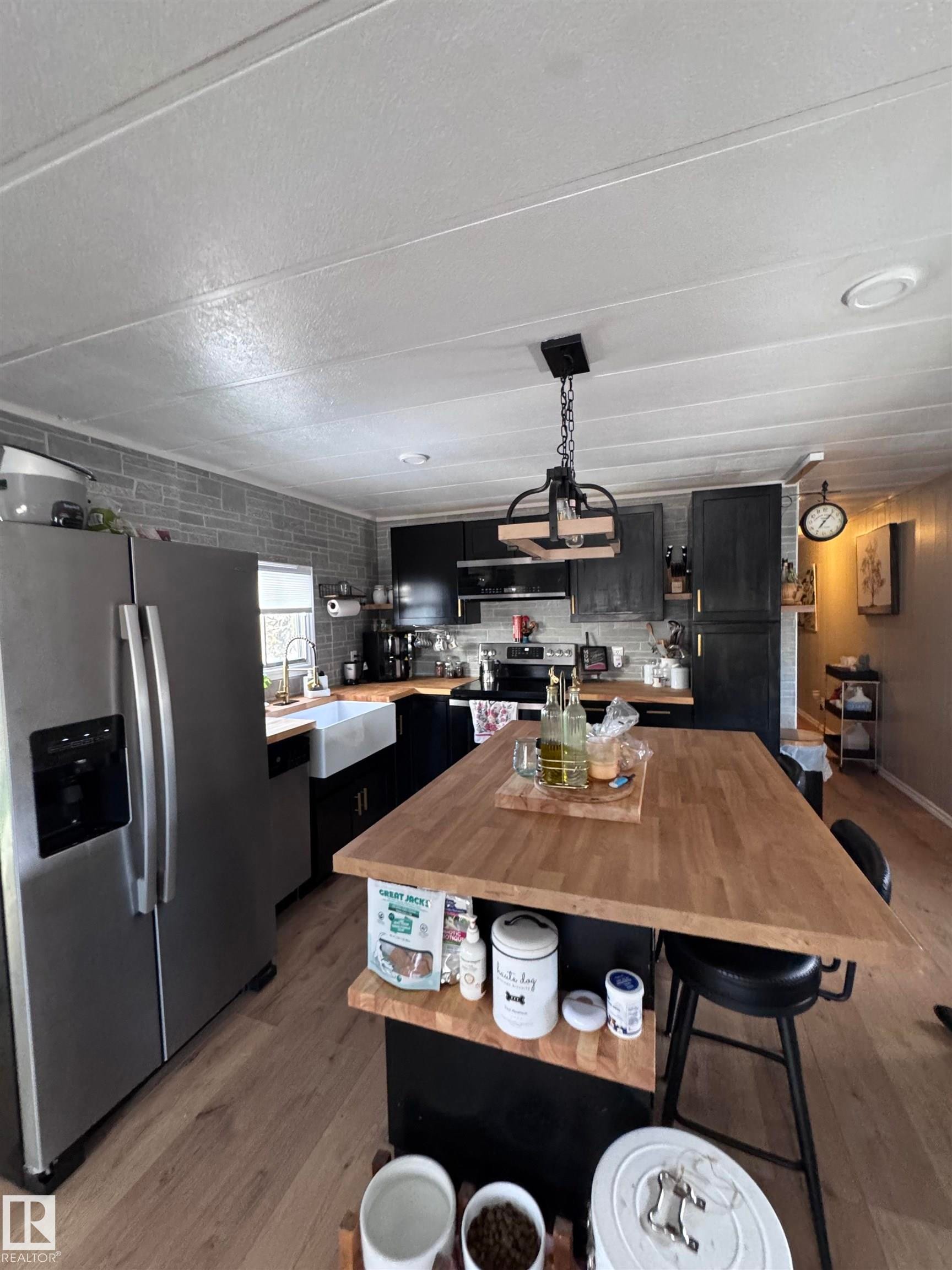 Kitchen with dark cabinets, stainless steel appliances, pendant lighting, a breakfast bar area, and light wood-type flooring - #44 9501 104 Ave, Westlock, AB - Indoor