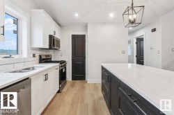 Kitchen with stainless steel appliances, light stone countertops, white cabinets, hanging light fixtures, and recessed lighting -
