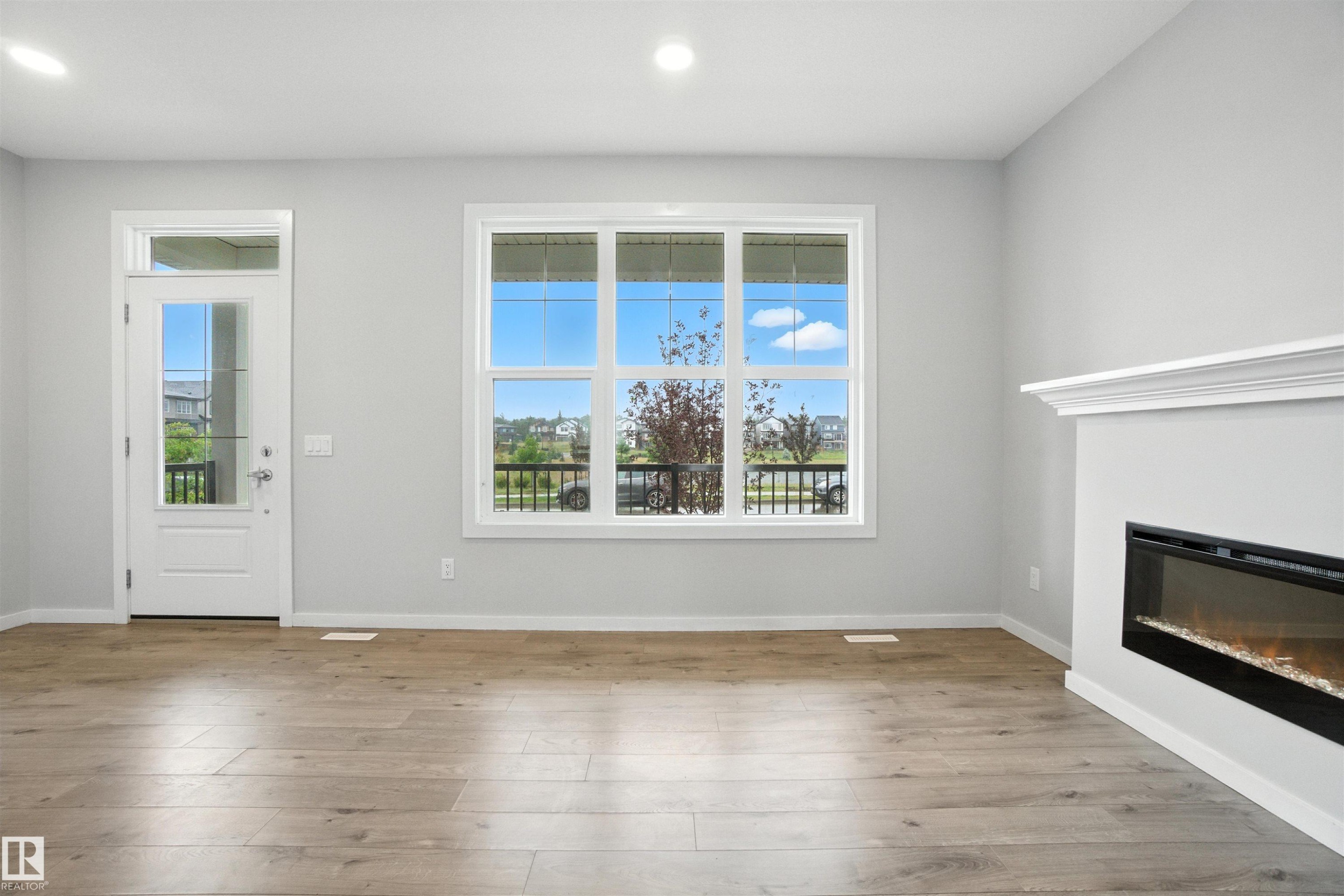 Unfurnished living room featuring healthy amount of natural light, a glass covered fireplace, light wood finished floors, and recessed lighting - 20727 25 Ave, Edmonton, AB - Indoor Photo Showing Other Room With Fireplace