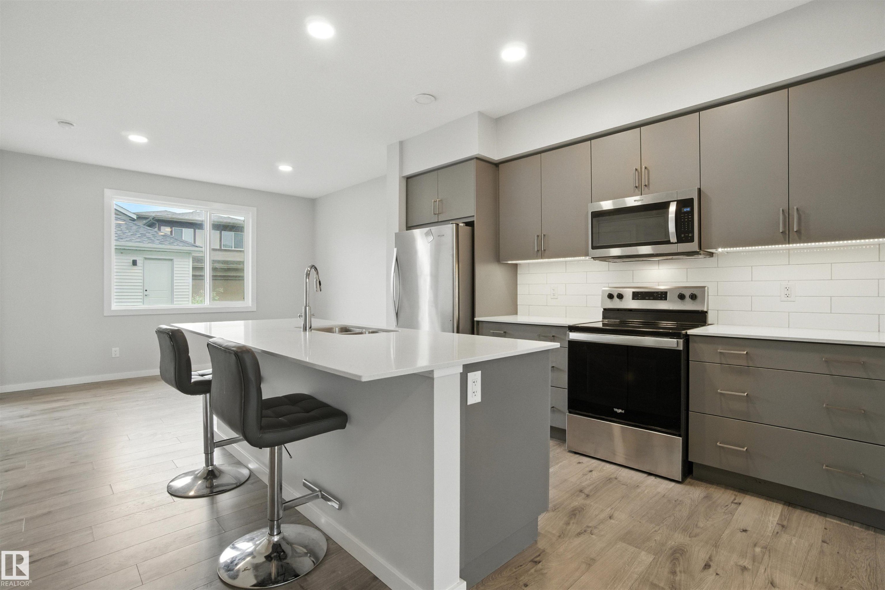 Kitchen with gray cabinets, tasteful backsplash, appliances with stainless steel finishes, light wood-style flooring, and recessed lighting - 20727 25 Ave, Edmonton, AB - Indoor Photo Showing Kitchen With Upgraded Kitchen