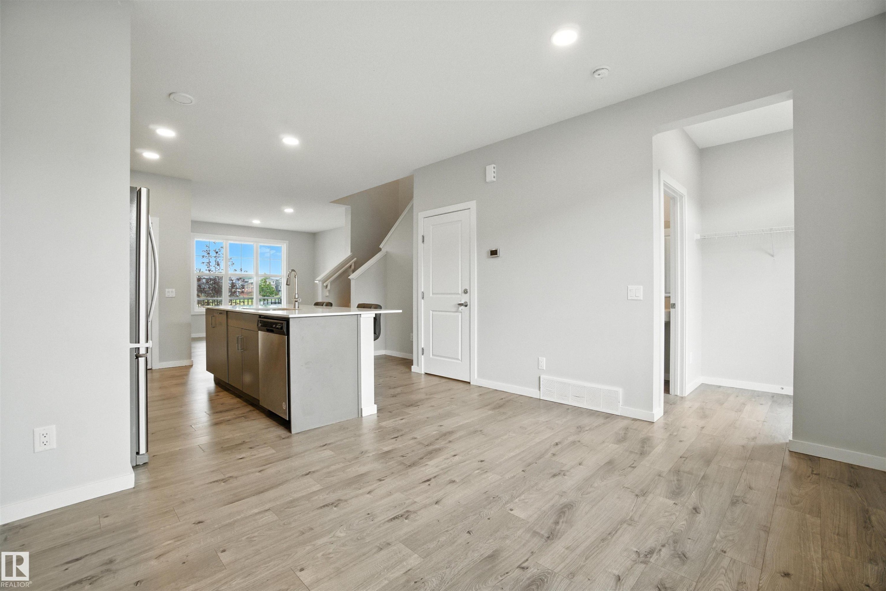 Kitchen with a center island with sink, recessed lighting, light wood-style floors, stainless steel appliances, and light stone counters - 20727 25 Ave, Edmonton, AB - Indoor Photo Showing Other Room