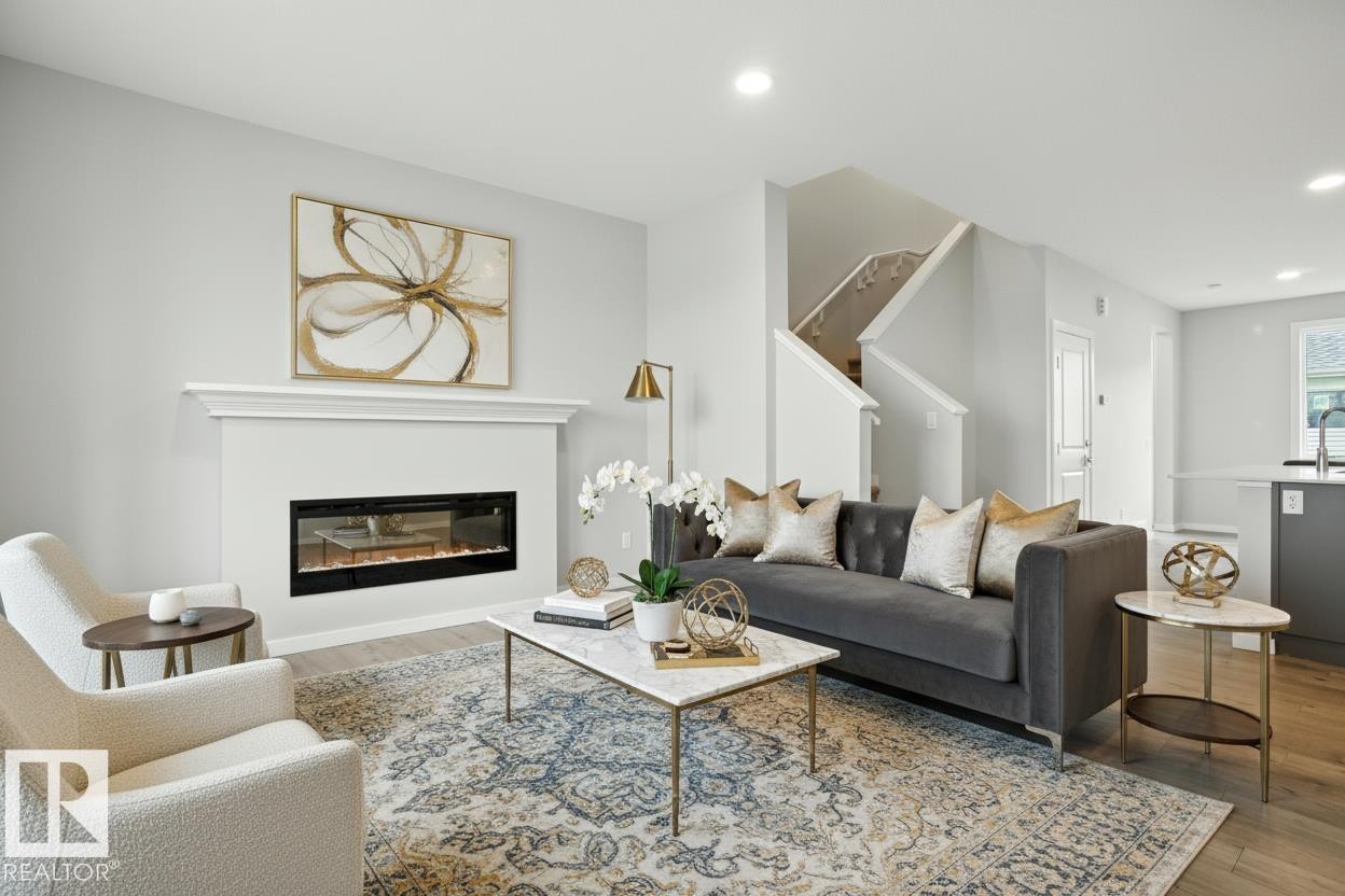 Living area with light wood finished floors, recessed lighting, and a glass covered fireplace - 20727 25 Ave, Edmonton, AB - Indoor Photo Showing Living Room With Fireplace