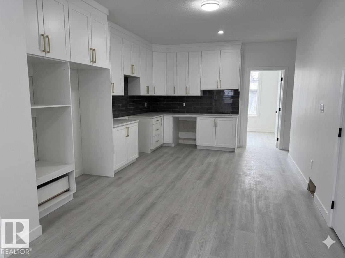 Kitchen featuring extensive white cabinetry with gold hardware, dark subway tile backsplash, and light wood-style flooring - 3605 112 Ave, Edmonton, AB - Indoor Photo Showing Kitchen