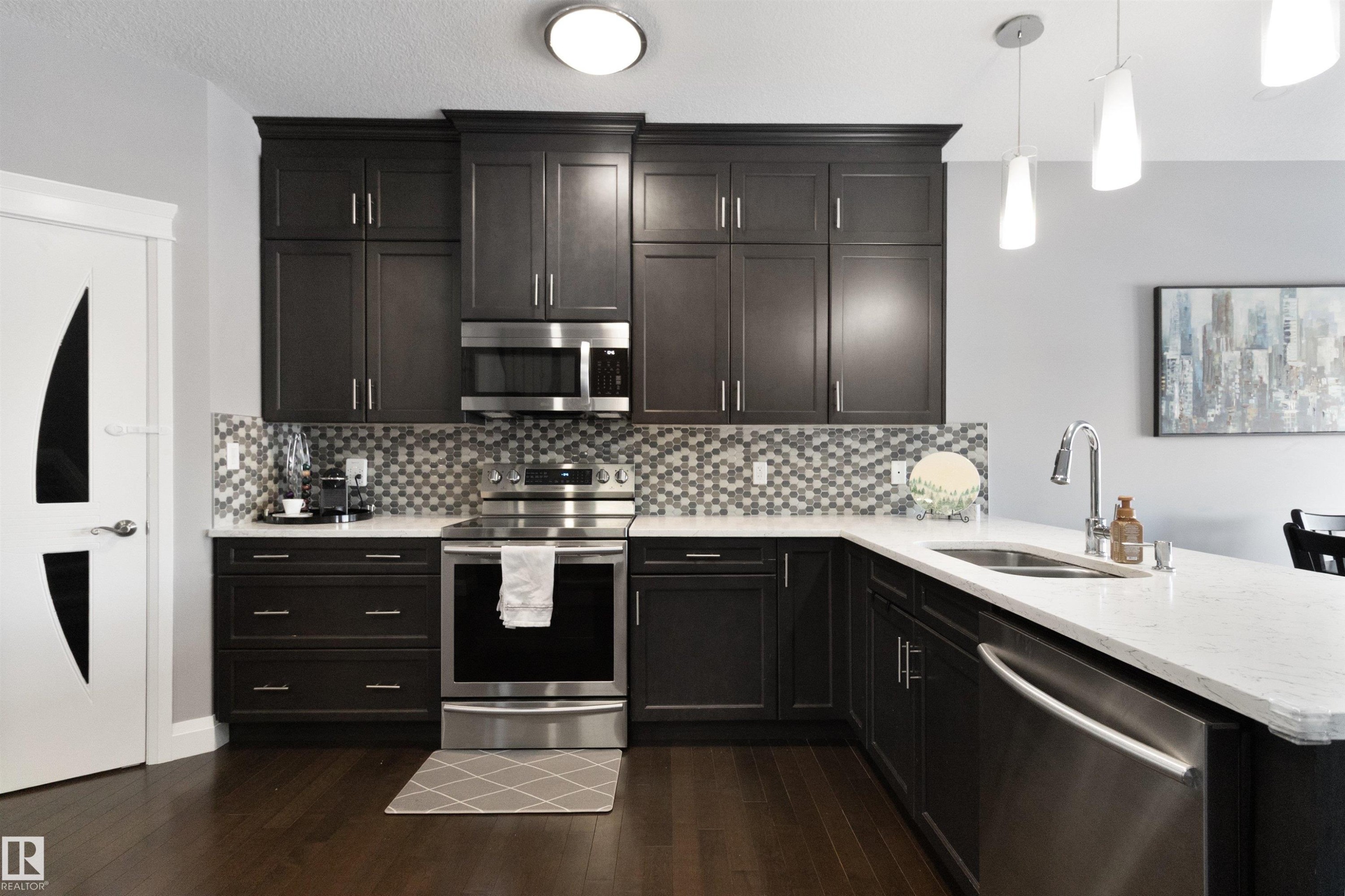 Kitchen with stainless steel appliances, light stone counters, hanging light fixtures, a peninsula, and dark wood-type flooring - 56 Durrand Bend, Fort Saskatchewan, AB - Indoor Photo Showing Kitchen With Double Sink With Upgraded Kitchen