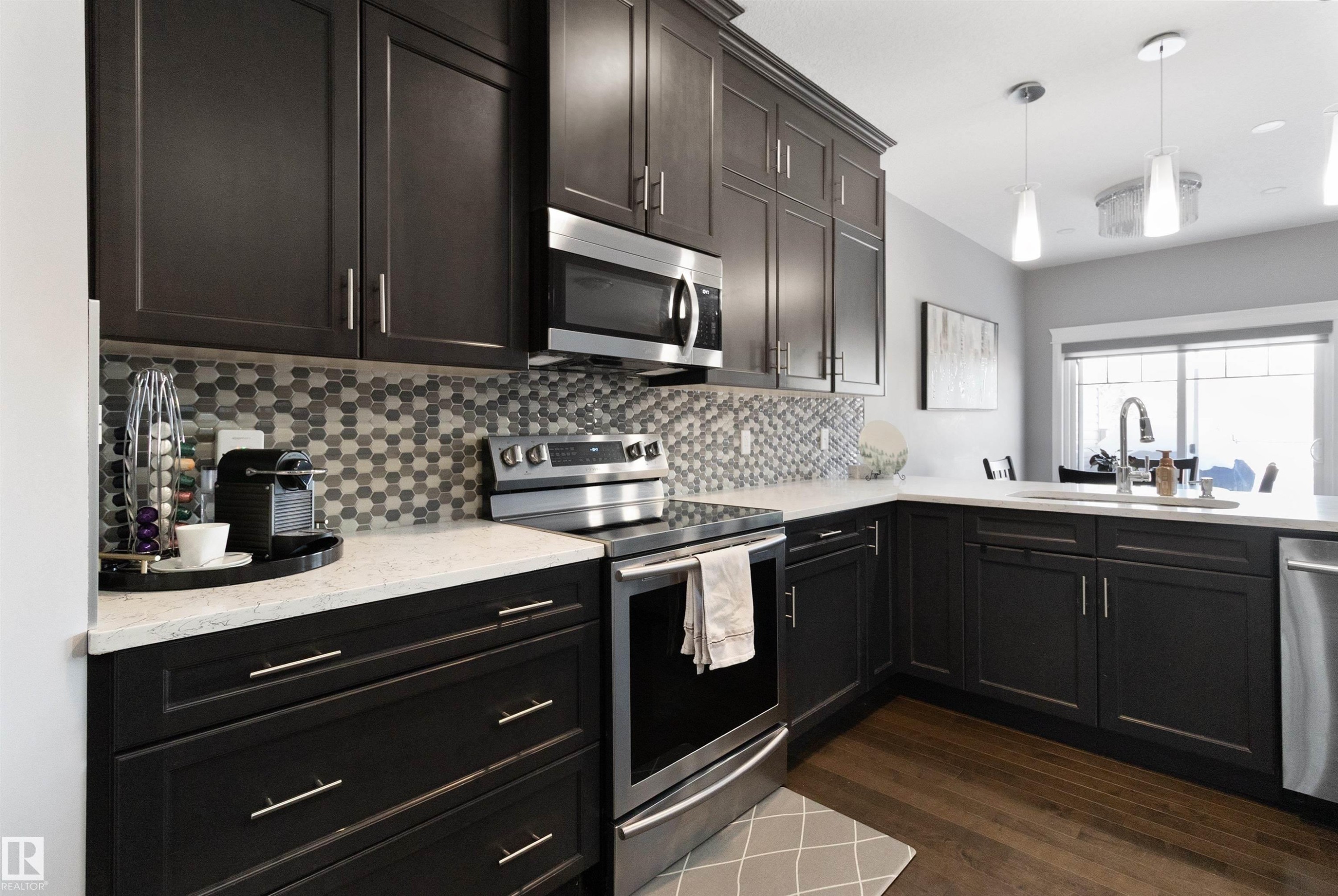 Kitchen featuring stainless steel appliances, dark wood-style floors, pendant lighting, light stone counters, and backsplash - 56 Durrand Bend, Fort Saskatchewan, AB - Indoor Photo Showing Kitchen With Upgraded Kitchen