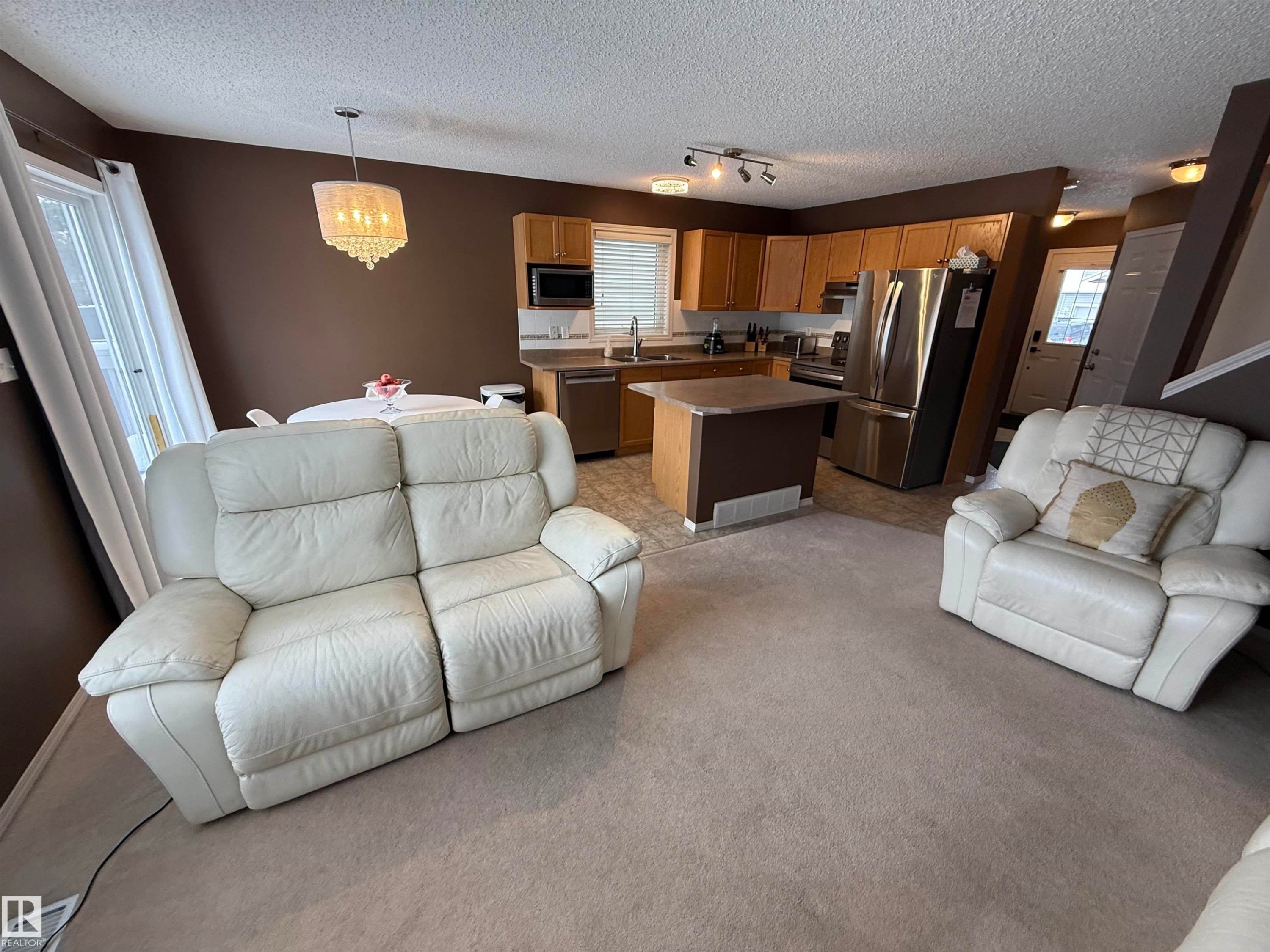Living area with a textured ceiling, light carpet, and hanging lights - 19 2021 Grantham Crest, Edmonton, AB - Indoor Photo Showing Living Room