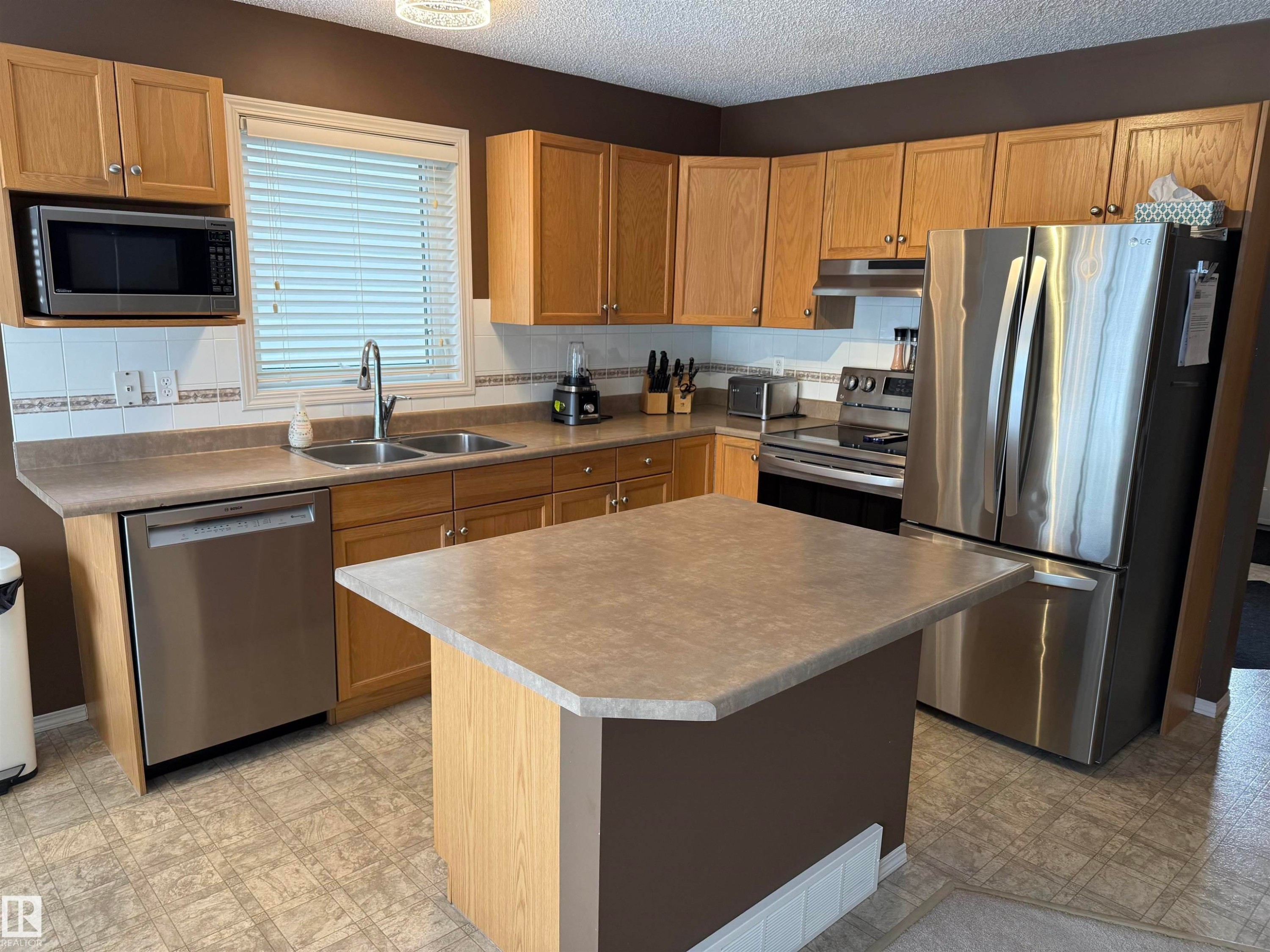 Kitchen with light floors, stainless steel appliances, a kitchen island, a textured ceiling, and light countertops - 19 2021 Grantham Crest, Edmonton, AB - Indoor Photo Showing Kitchen With Stainless Steel Kitchen With Double Sink
