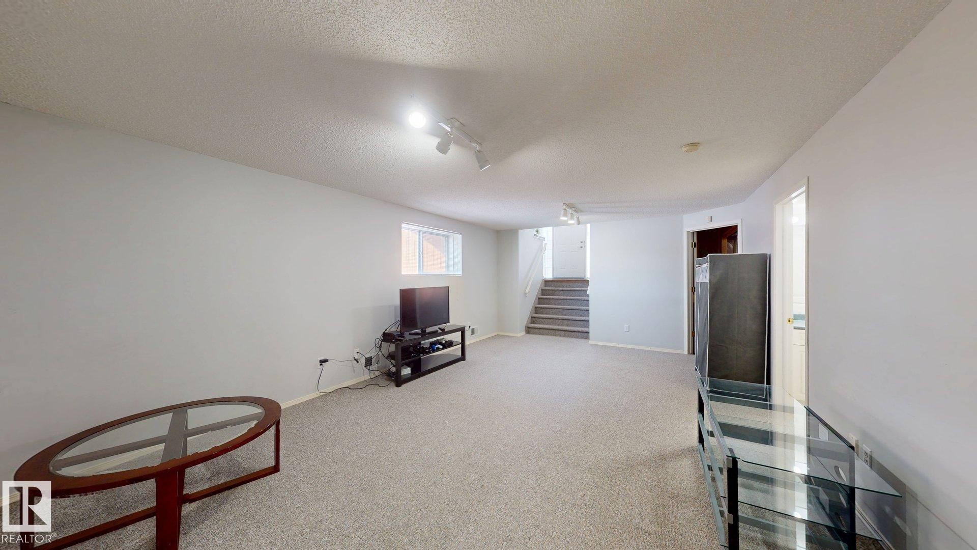 Basement with rail lighting, a textured ceiling, and light colored carpet - 17010 84 Street, Edmonton, AB - Indoor