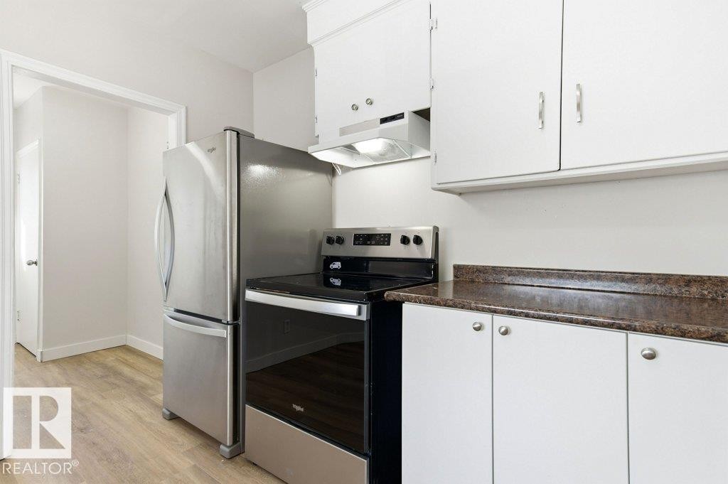 Kitchen featuring stainless steel appliances, white cabinetry, and dark countertops - 10704 96 St Nw, Edmonton, AB - Indoor Photo Showing Kitchen
