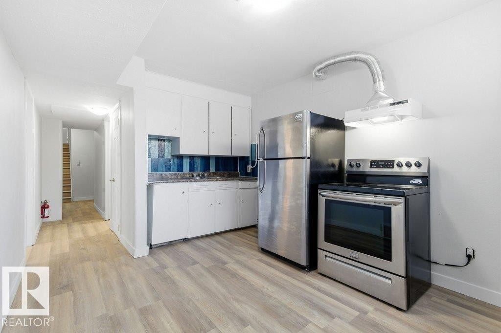 Kitchen with stainless steel appliances, white cabinets, exhaust hood, light wood-style flooring, and dark countertops - 10704 96 St Nw, Edmonton, AB - Indoor Photo Showing Kitchen