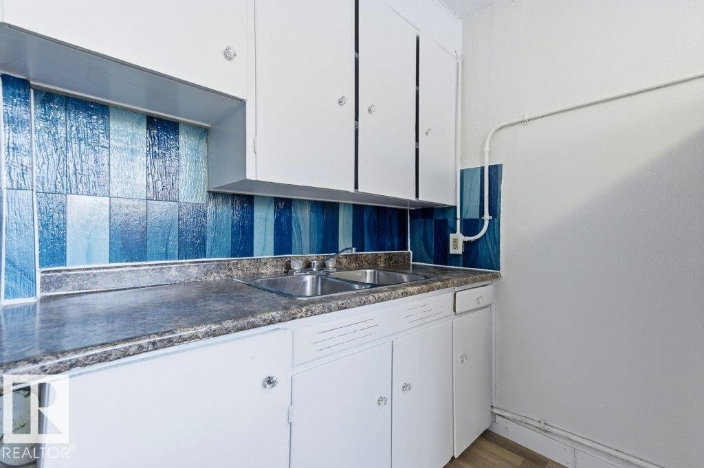 Kitchen with white cabinets, dark countertops, and light wood-style flooring - 10704 96 St Nw, Edmonton, AB - Indoor Photo Showing Kitchen With Double Sink