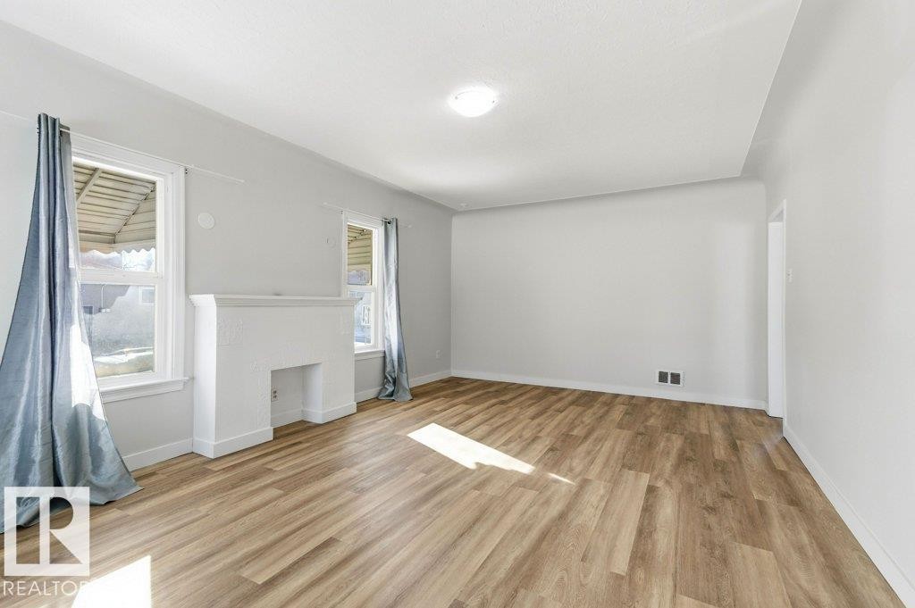 Unfurnished living room featuring light wood finished floors and a fireplace - 10704 96 St Nw, Edmonton, AB - Indoor Photo Showing Other Room
