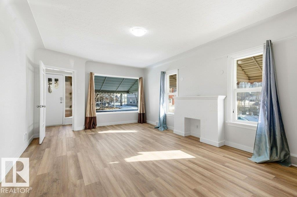 Unfurnished living room featuring light wood-style floors and a fireplace - 10704 96 St Nw, Edmonton, AB - Indoor