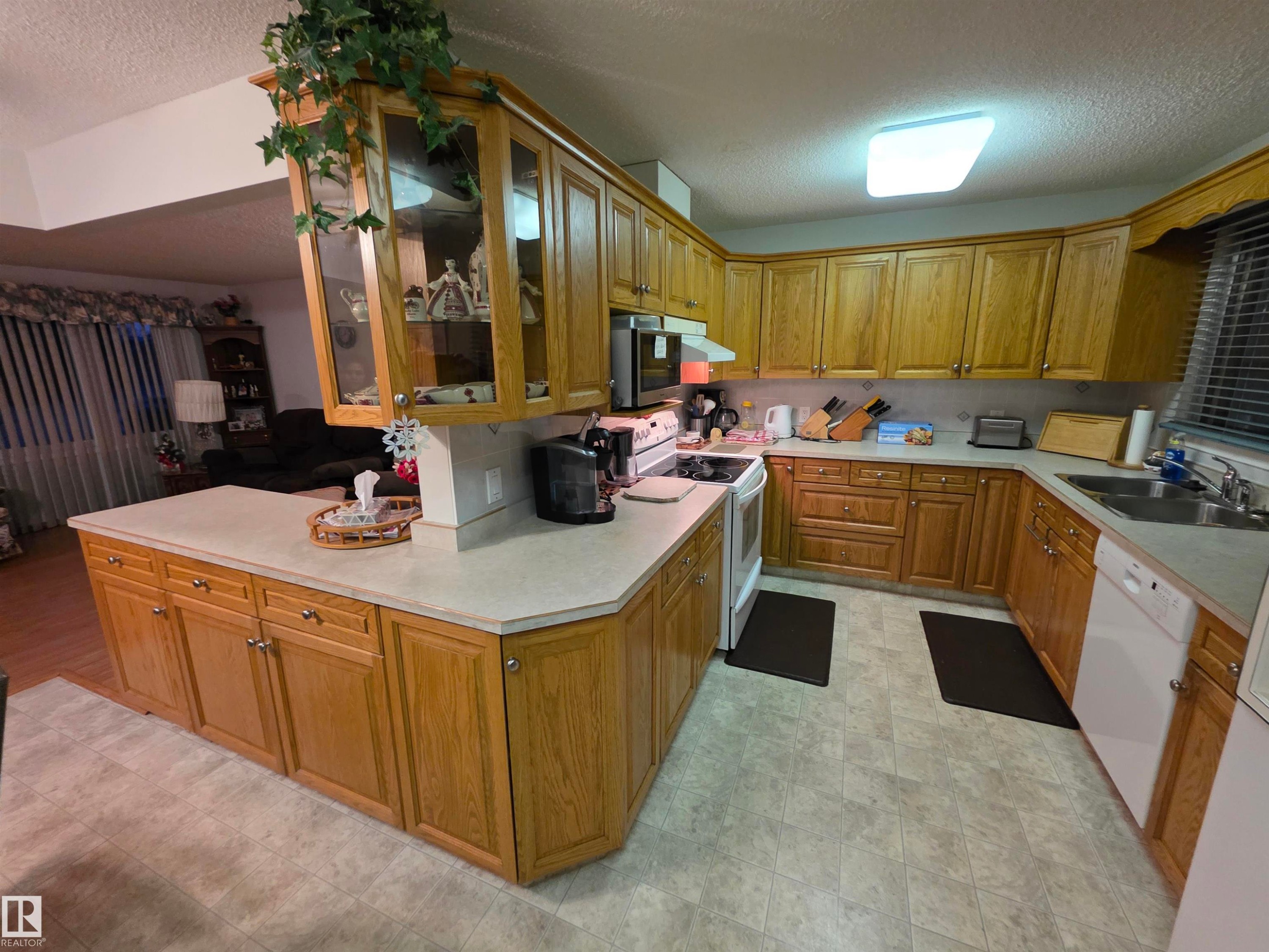 Kitchen featuring a textured ceiling, light countertops, white appliances, glass fronted cabinets, and wood finish cabinets - 4400 45 Avenue, Stony Plain, AB - Indoor Photo Showing Kitchen