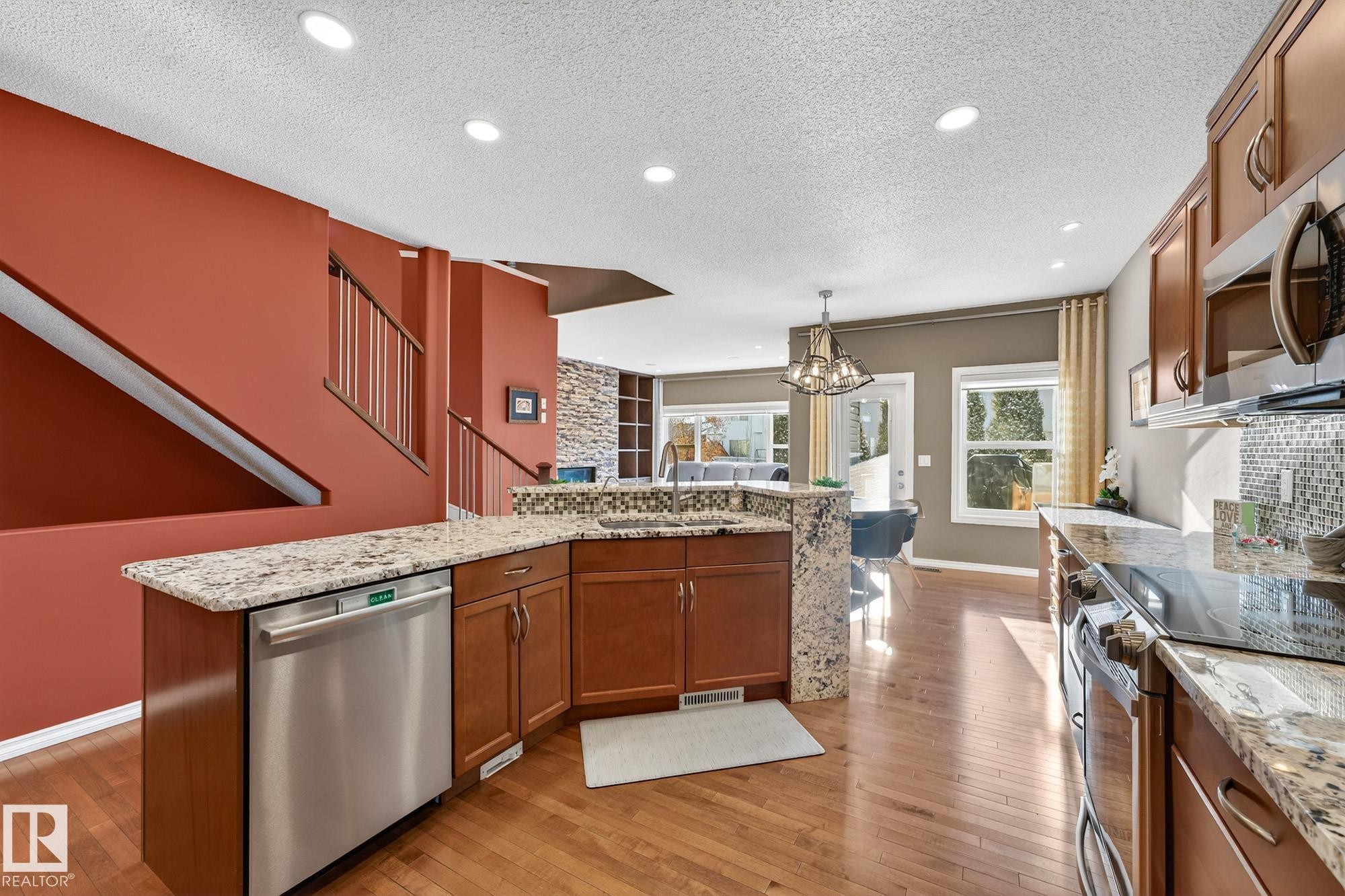 Kitchen featuring wood finish cabinets, stainless steel appliances, light stone counters, light wood finished floors, and a textured ceiling - 2036 Hilliard Place, Edmonton, AB - Indoor Photo Showing Kitchen