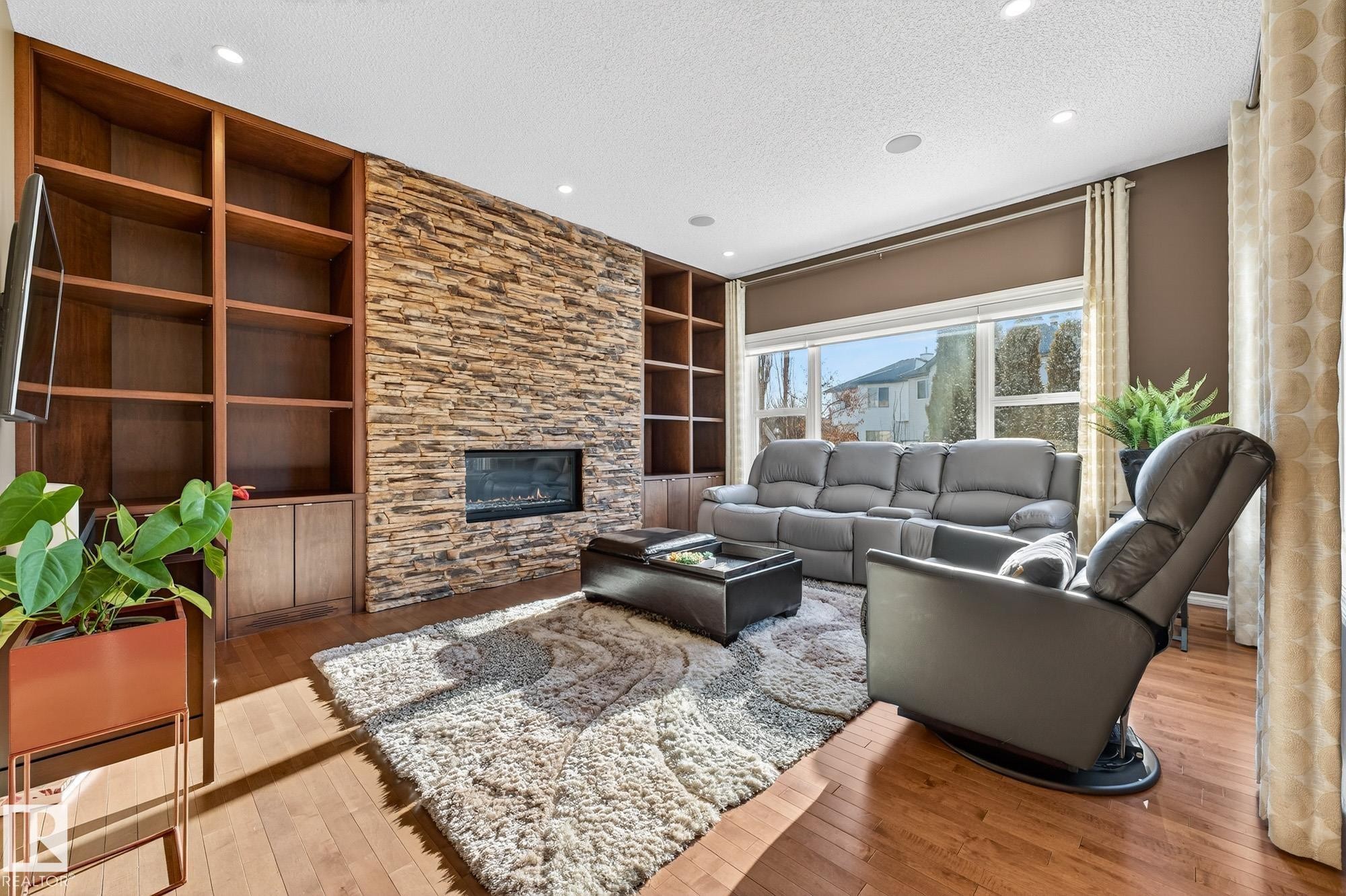 Living room featuring built in features, wood-type flooring, a textured ceiling, a fireplace, and recessed lighting - 2036 Hilliard Place, Edmonton, AB - Indoor Photo Showing Living Room With Fireplace