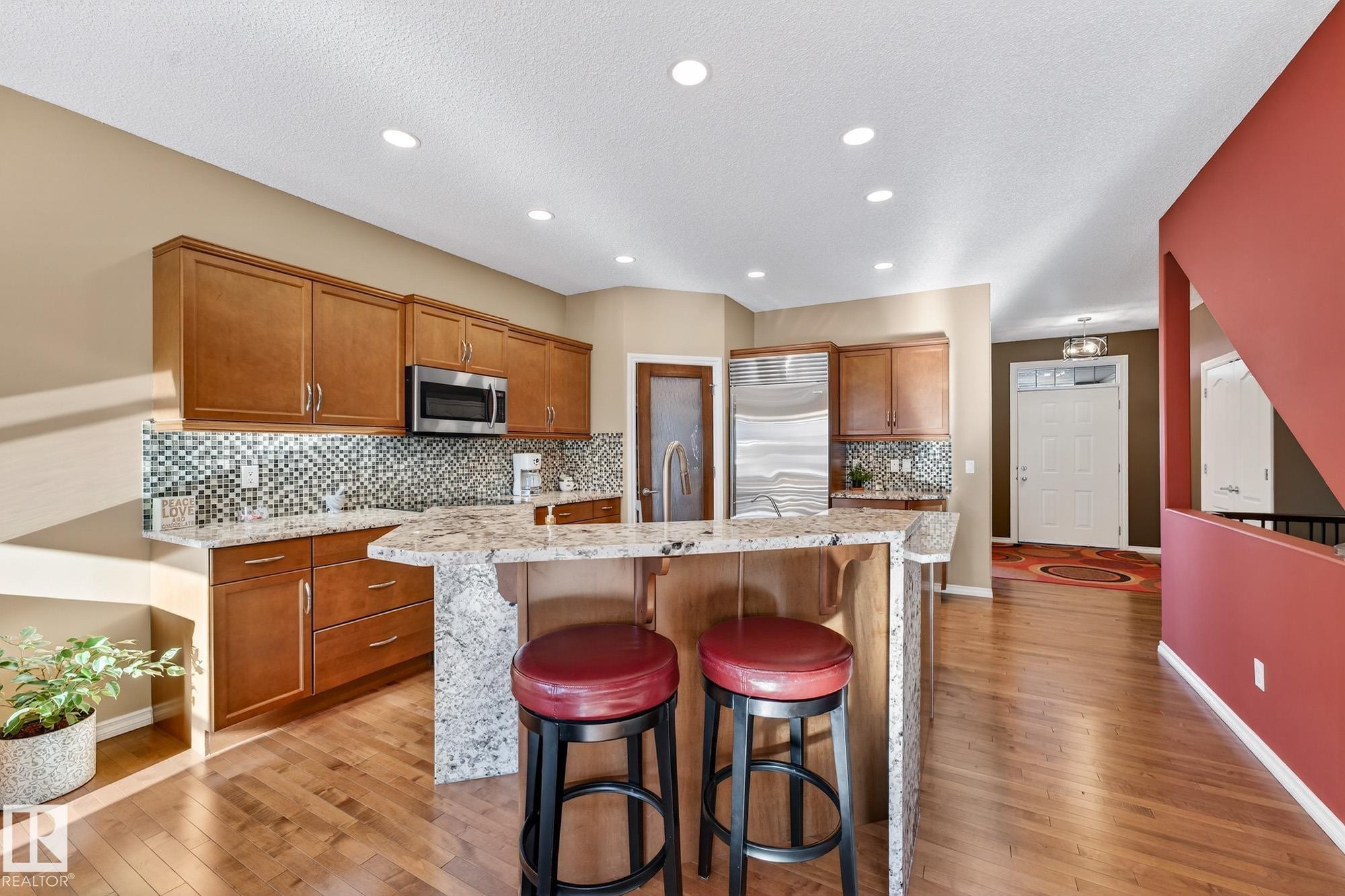Kitchen with a breakfast bar area, wood finish cabinetry, light stone counters, backsplash, and an island with sink - 2036 Hilliard Place, Edmonton, AB - Indoor Photo Showing Kitchen With Upgraded Kitchen