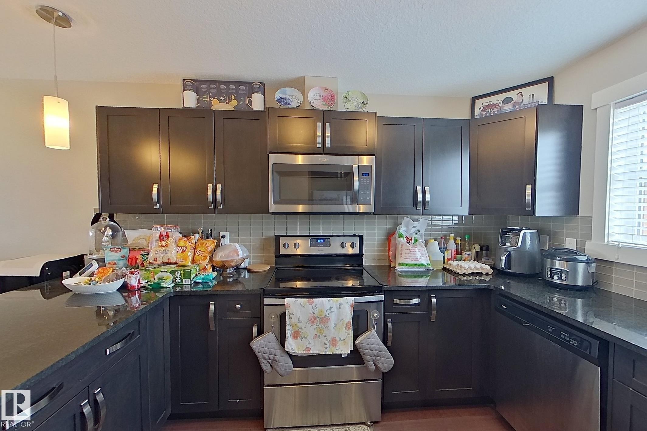 Kitchen featuring stainless steel appliances, dark stone countertops, pendant lighting, and backsplash - 295 401 Southfork Drive, Leduc, AB - Indoor Photo Showing Kitchen With Stainless Steel Kitchen With Upgraded Kitchen