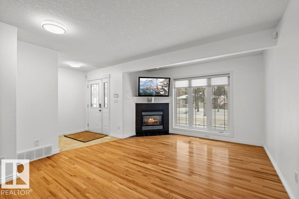 Unfurnished living room with a textured ceiling, a tile fireplace, healthy amount of natural light, and light wood-type flooring - 10639 70 Avenue, Edmonton, AB - Indoor Photo Showing Living Room With Fireplace