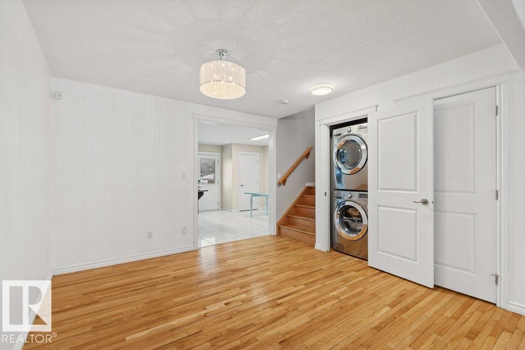 Laundry room featuring light wood-style floors, estacked washer and dryer, and a chandelier - 10639 70 Avenue, Edmonton, AB - Indoor Photo Showing Laundry Room