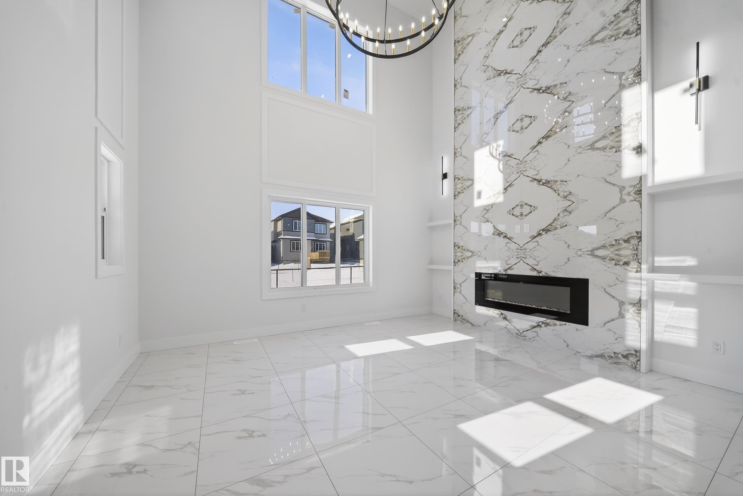 Unfurnished living room featuring a high end fireplace, a high ceiling, a chandelier, and light marble finish floors - 4006 40 Street, Beaumont, AB - Indoor With Fireplace