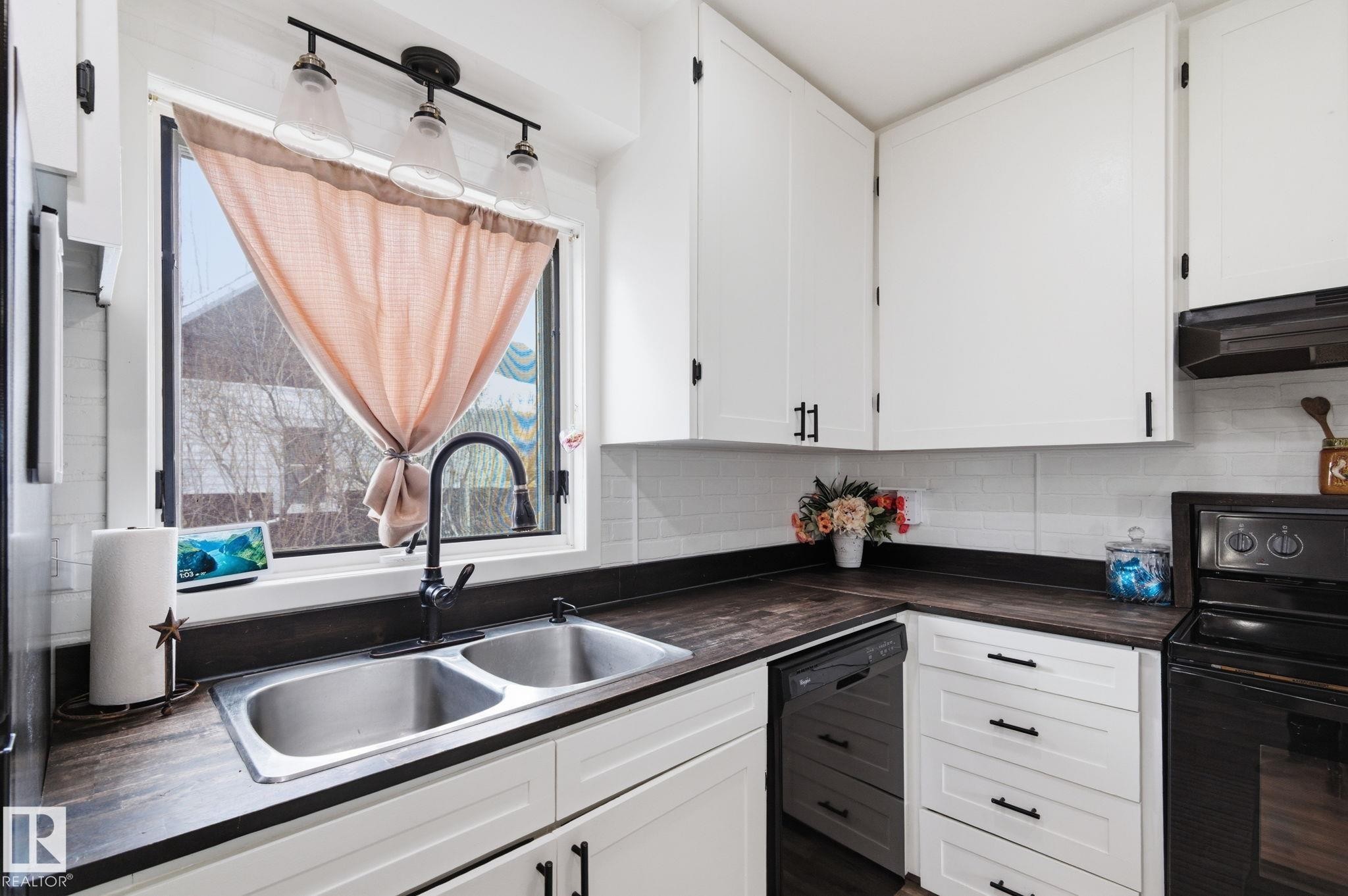 Kitchen featuring black appliances, dark countertops, white cabinetry, and decorative backsplash - 4919 50 Avenue, Bon Accord, AB - Indoor Photo Showing Kitchen With Double Sink