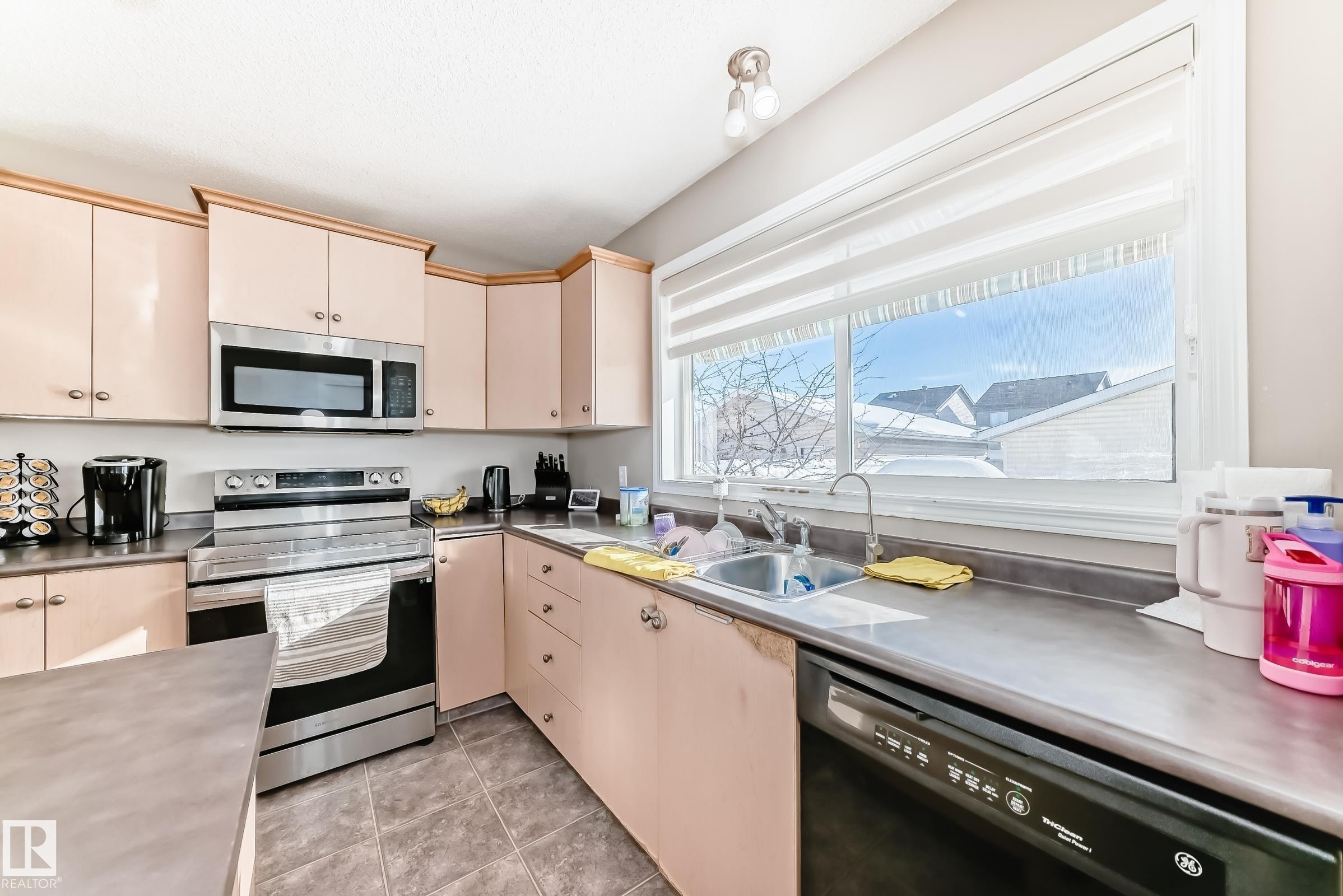 Kitchen featuring stainless steel countertops, stainless steel appliances, and cream cabinetry - 14043 151 Avenue, Edmonton, AB - Indoor Photo Showing Kitchen With Double Sink