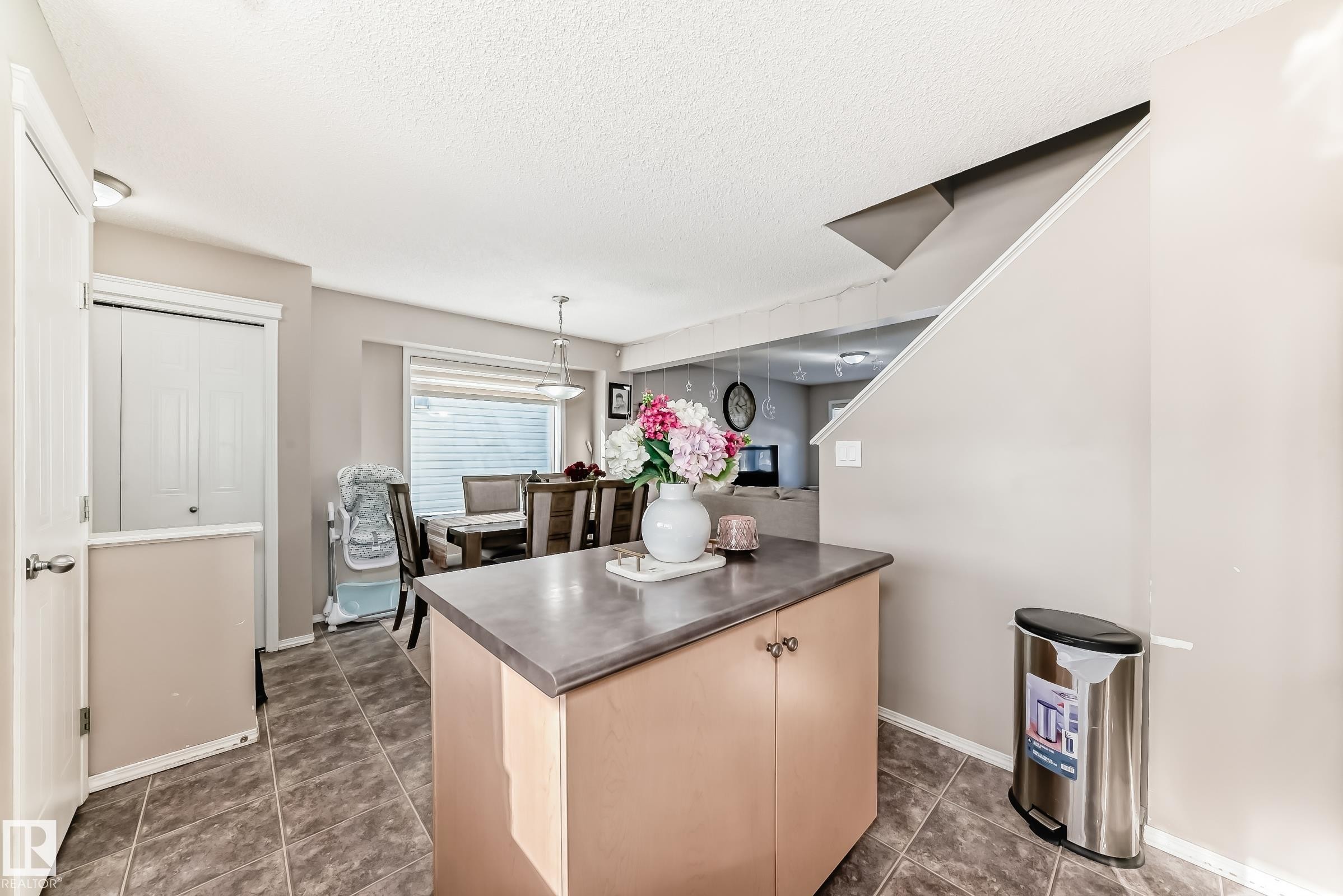 Kitchen featuring decorative light fixtures, light wood finish cabinets, a textured ceiling, dark tile patterned floors, and stainless steel counters - 14043 151 Avenue, Edmonton, AB - Indoor