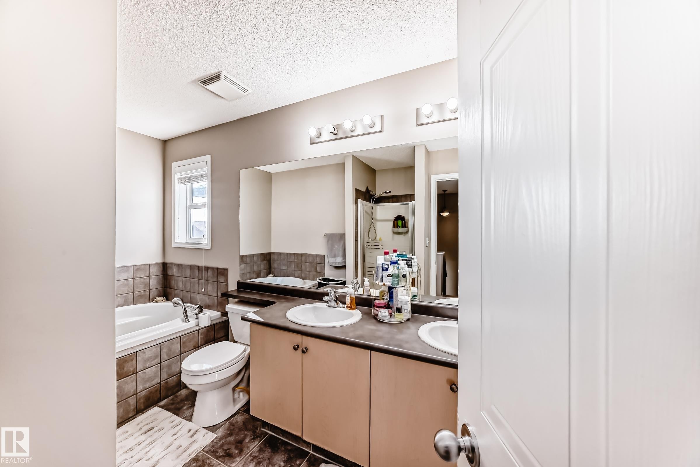 Full bath with double vanity, a garden tub, a textured ceiling, a shower stall, and dark tile patterned flooring - 14043 151 Avenue, Edmonton, AB - Indoor Photo Showing Bathroom