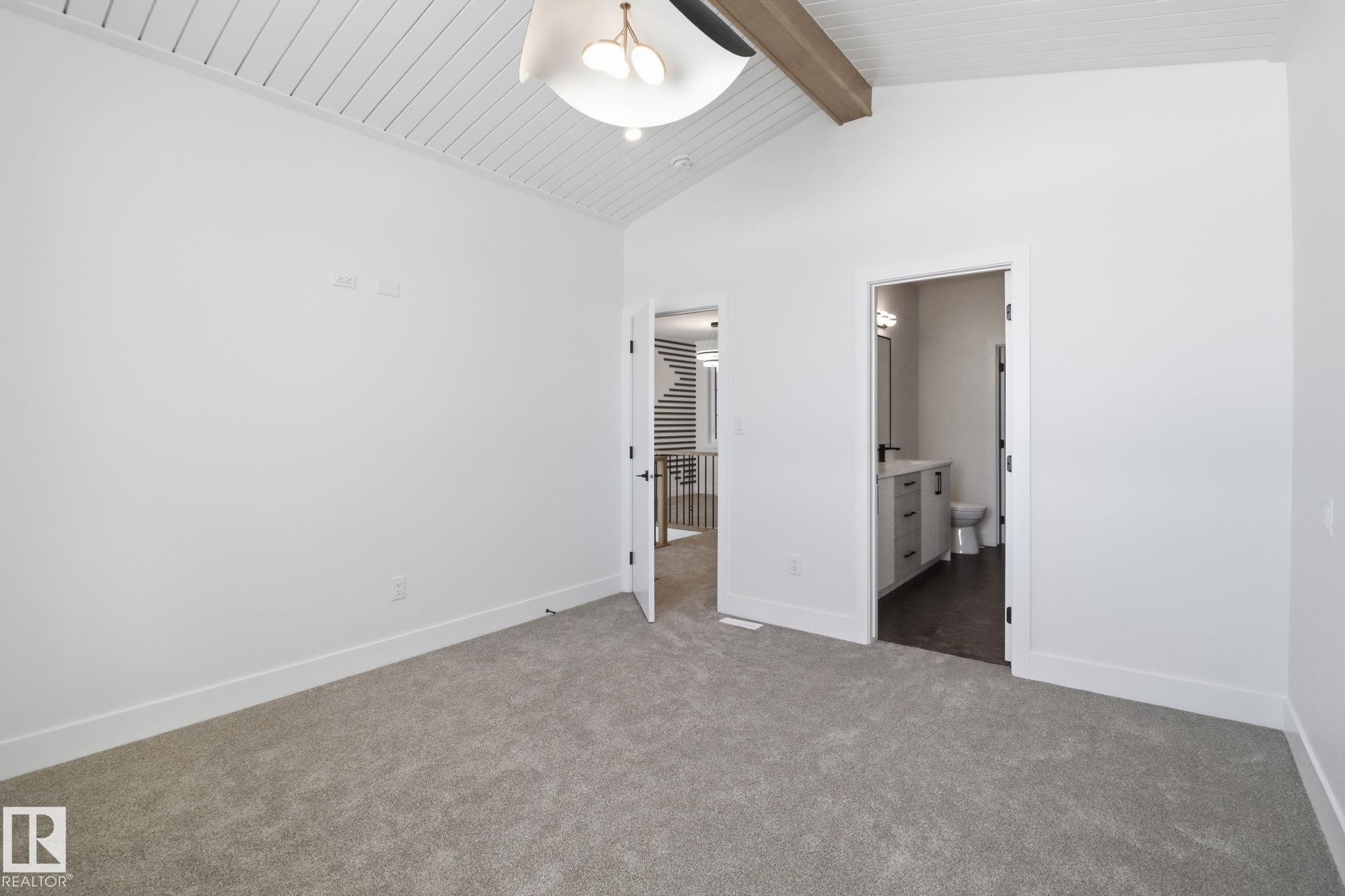 Unfurnished bedroom with dark colored carpet, connected bathroom, a ceiling fan, and a high wood beamed ceiling - 90 Eldridge Point(E), St. Albert, AB - Indoor Photo Showing Other Room