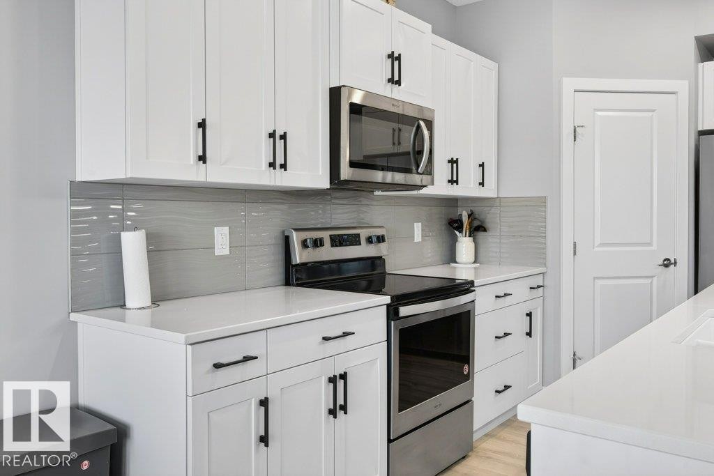 Kitchen featuring stainless steel appliances, modern cabinetry, stunning tile backsplash, and white quartz countertops. - 1909 Davidson Wynd, Edmonton, AB - Indoor Photo Showing Kitchen With Upgraded Kitchen