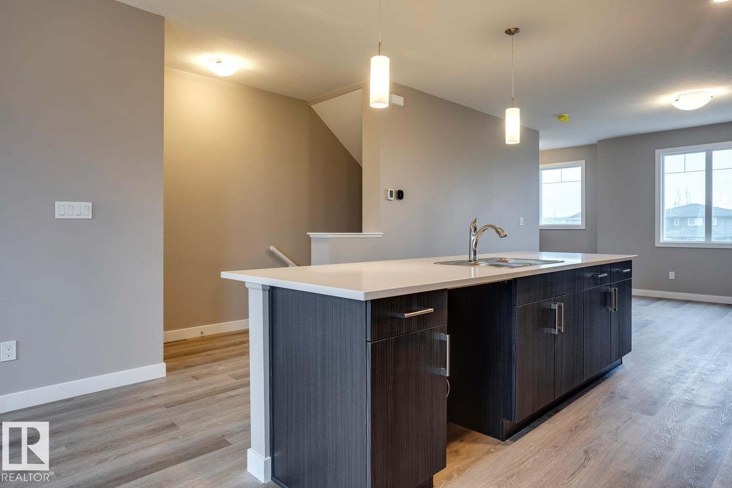 Kitchen with light wood-type flooring, modern cabinets, decorative light fixtures, an island with sink, and dark wood finish cabinetry - 78 13139 205 Street Nw, Edmonton, AB - Indoor Photo Showing Kitchen