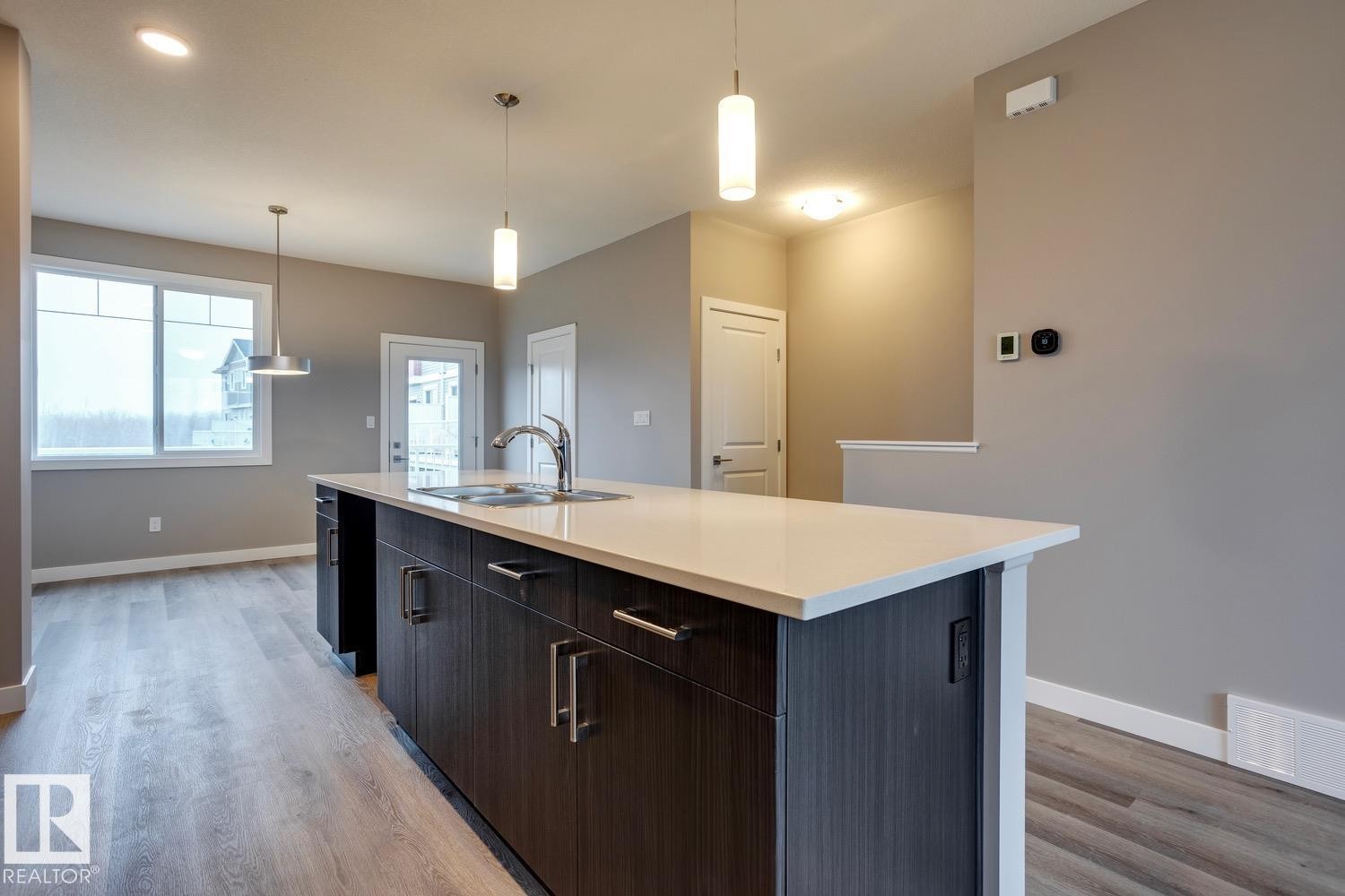 Kitchen with hanging light fixtures, a center island with sink, light wood-type flooring, and dark wood finish cabinetry - 78 13139 205 Street Nw, Edmonton, AB - Indoor Photo Showing Kitchen