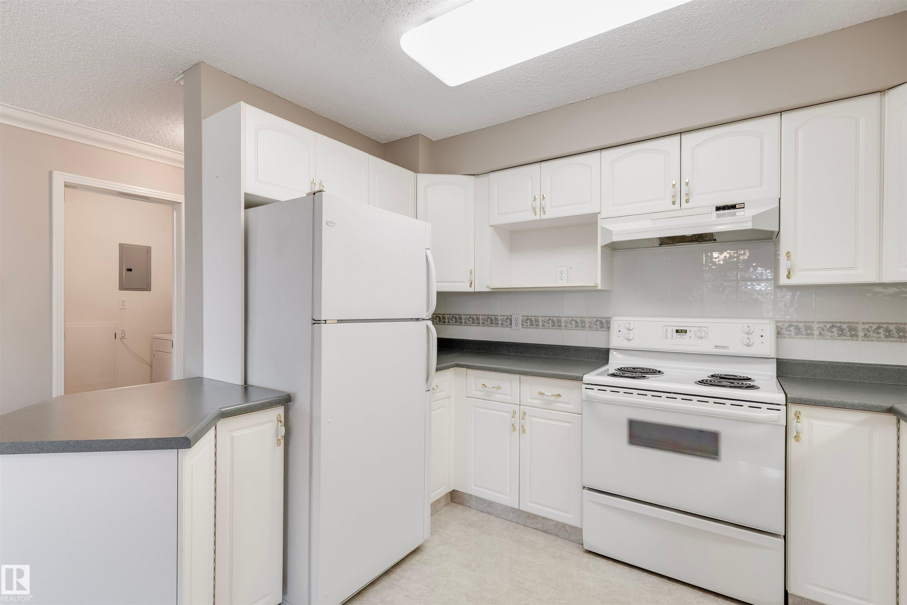 Kitchen featuring white appliances, a textured ceiling, white cabinets, and under cabinet range hood - 209 17150 94A Avenue, Edmonton, AB - Indoor Photo Showing Kitchen